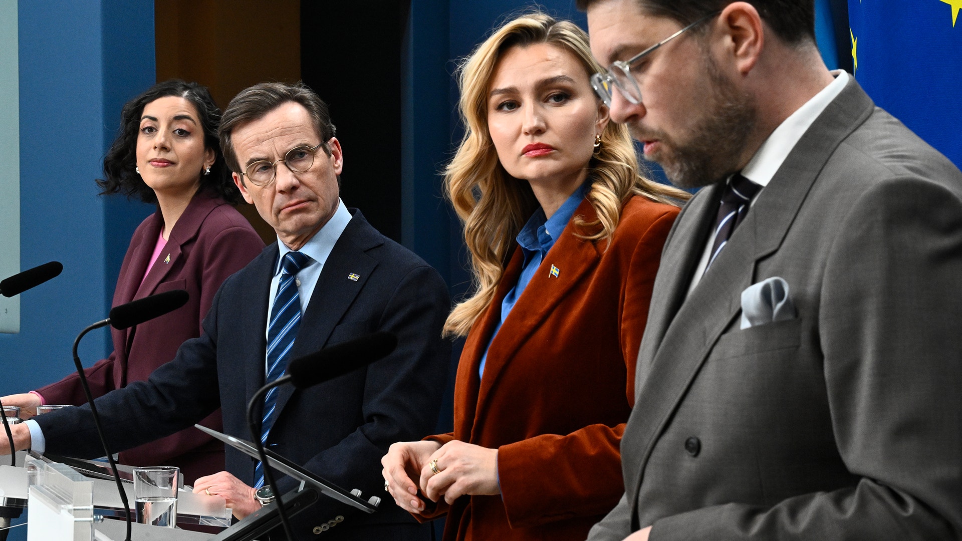 Fyra personer i formell klädsel sitter vid ett bord med mikrofoner under en presskonferens eller officiell sammankomst.