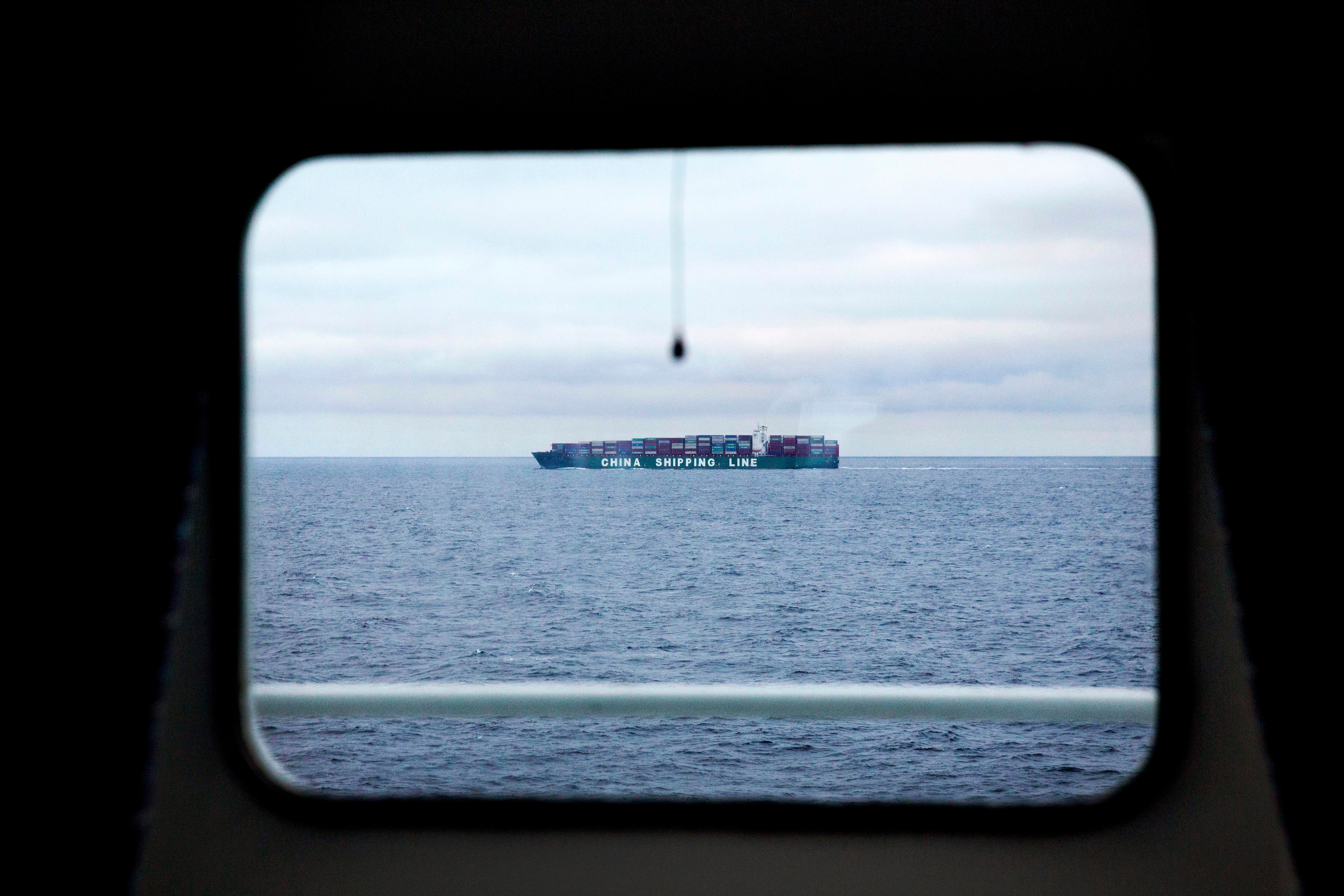 Ett containerfartyg på havet, fotograferat genom ett fönster eller en öppning.