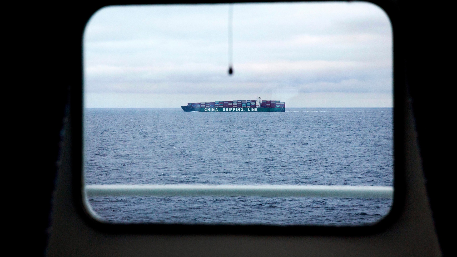 Ett containerfartyg på havet, fotograferat genom ett fönster eller en öppning.