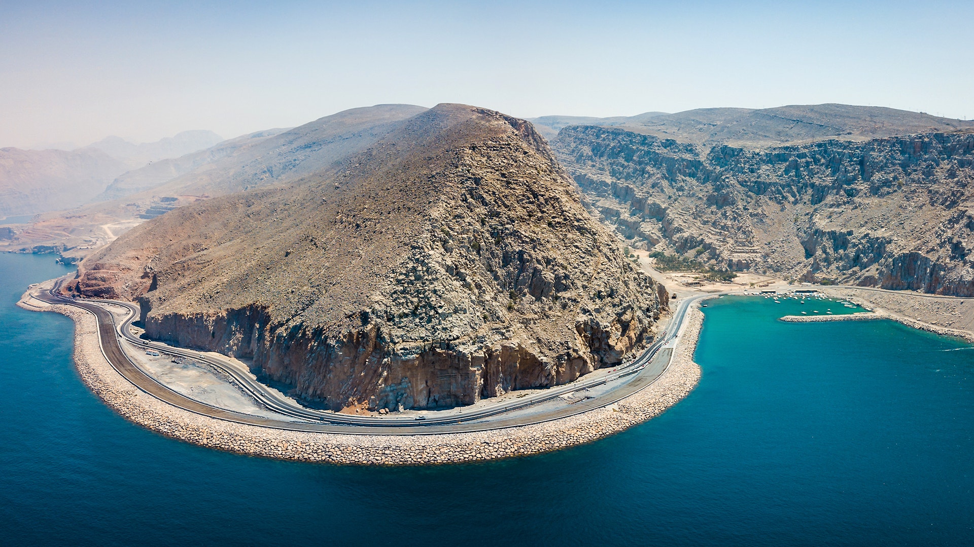 Luftfoto av Hormuz-halvön med stenig bergsformation omgiven av turkosblått vatten och en väg som löper runt kusten.