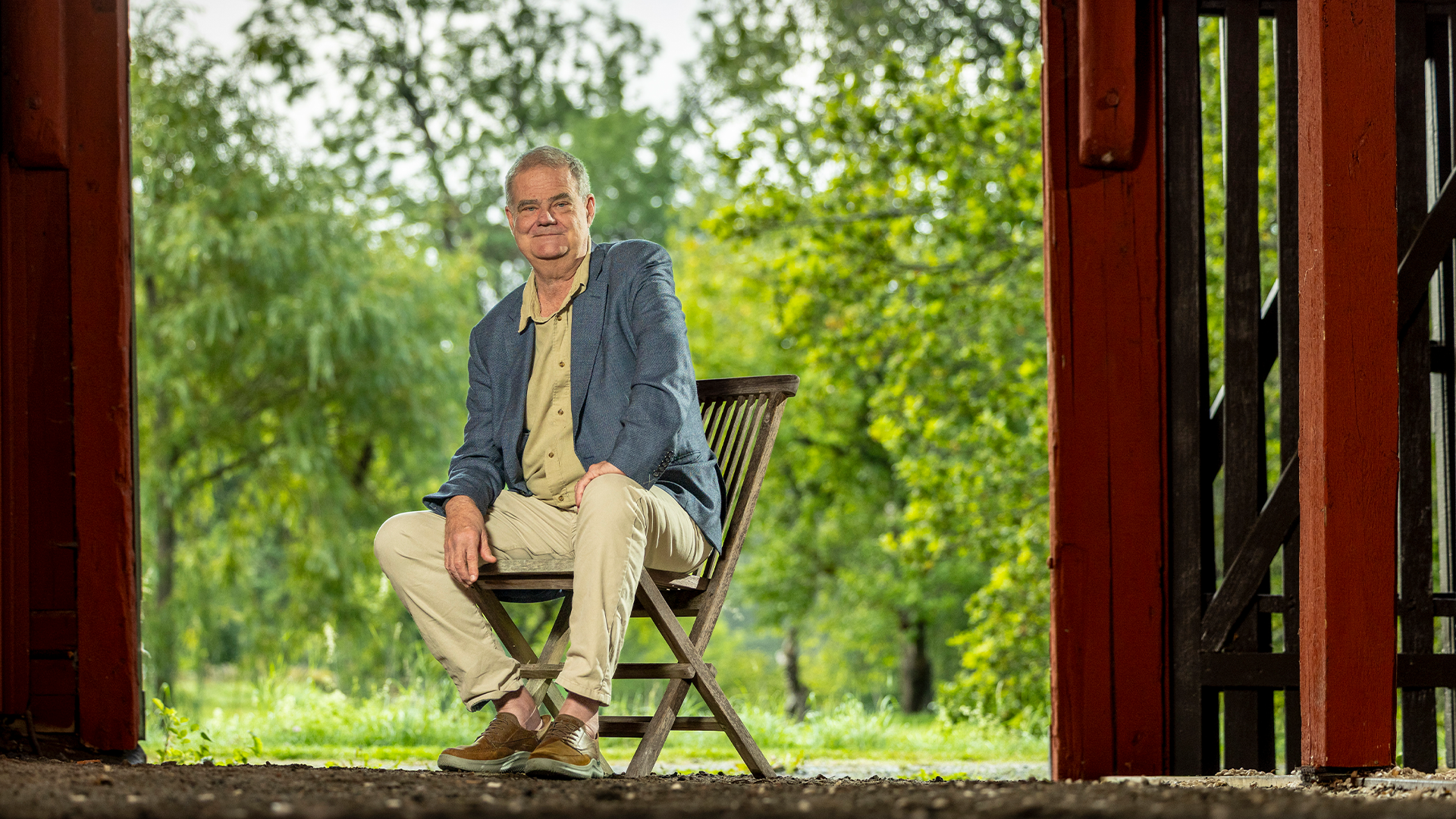 Martin Nordin sitter på en stol i en lada. Bakom honom är det grönt av buskar och träd.