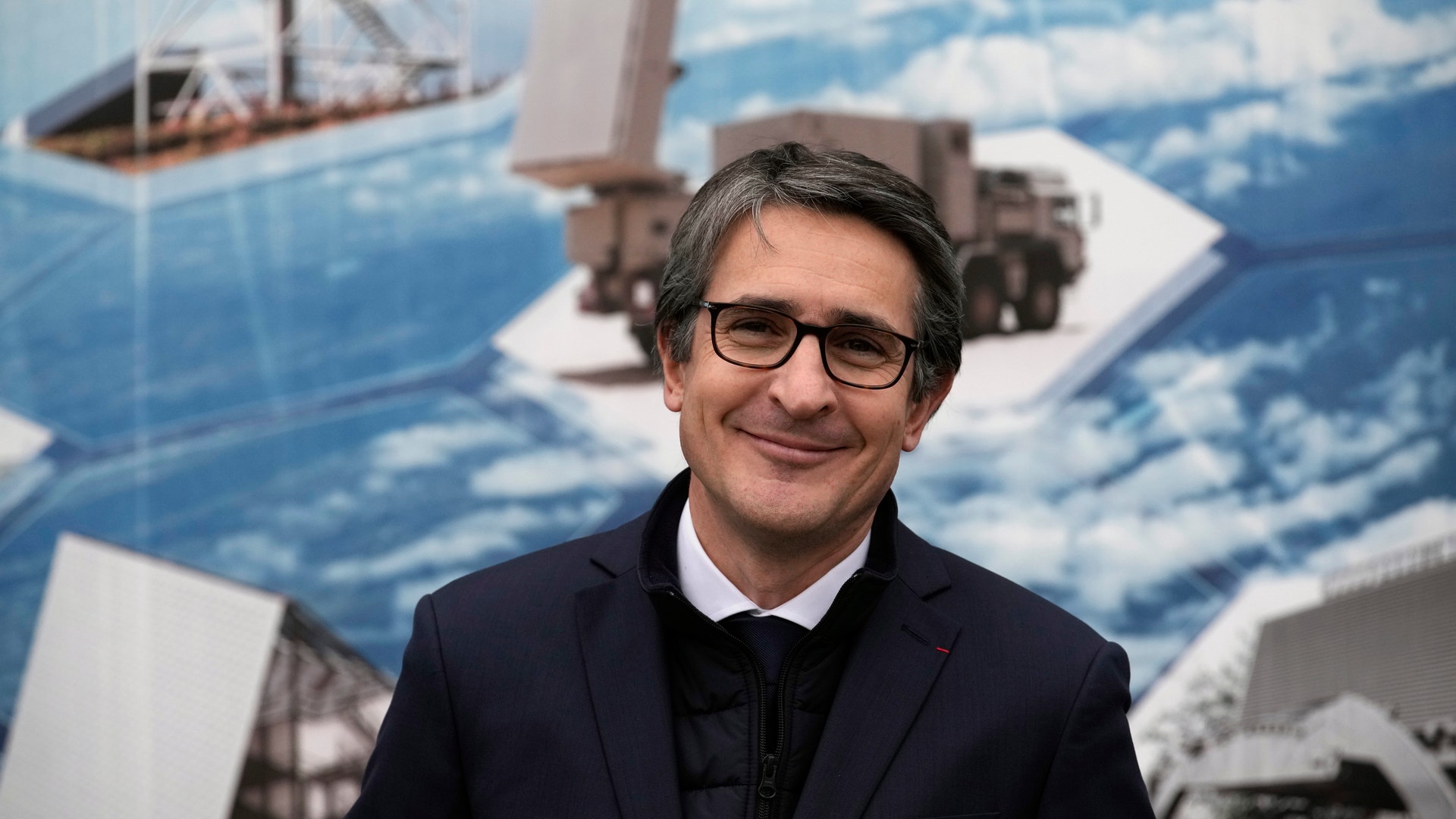 Porträtt av en man i kostym framför en bakgrund med bilder av fartyg och hav.