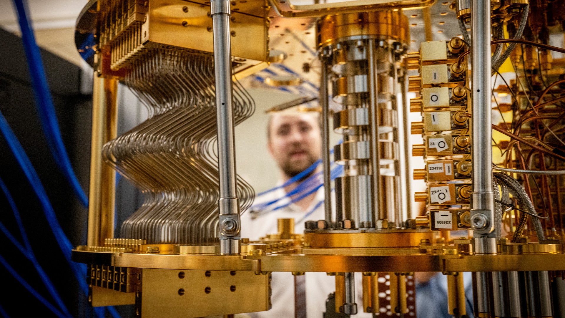 Inre komponenter av en kvantdator med gyllene metallram, komplexa ledningar och kylutrustning. En person syns i bakgrunden.