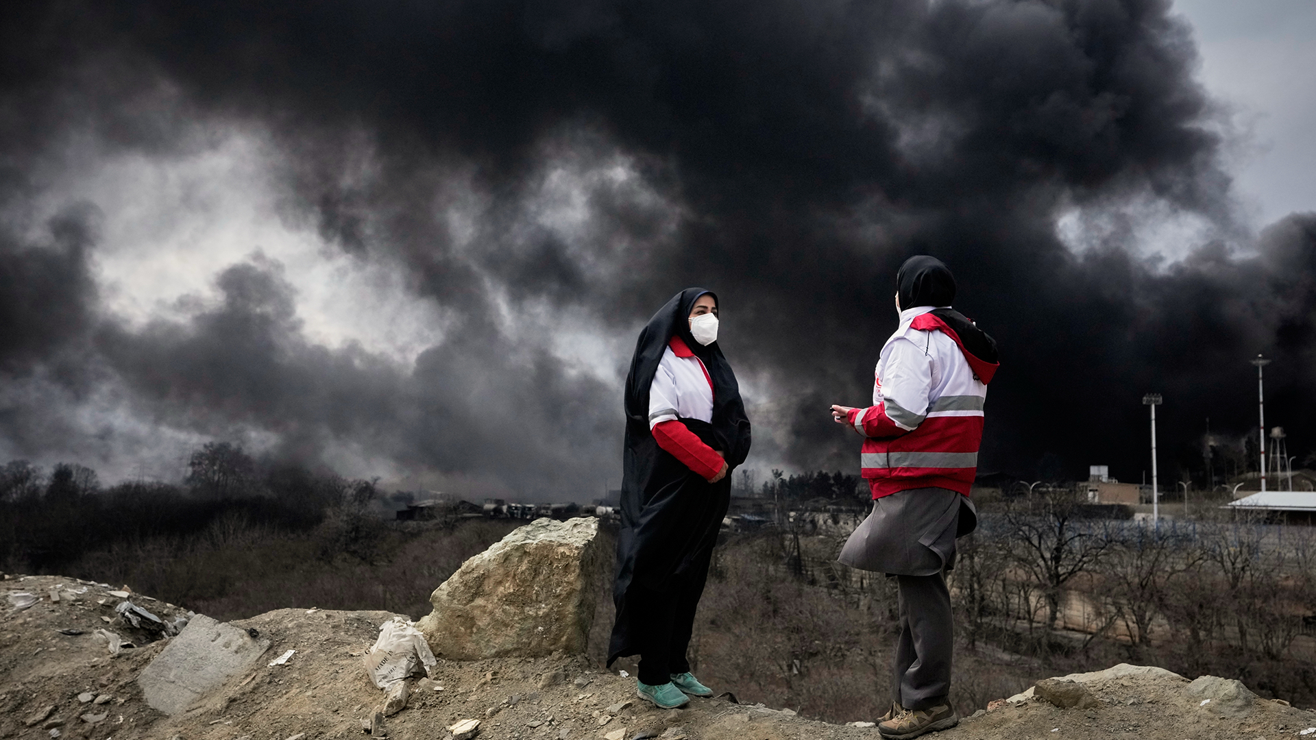 Två personer i röd och vit kläder står på en höjd med mörka stormmoln på himlen bakom sig.