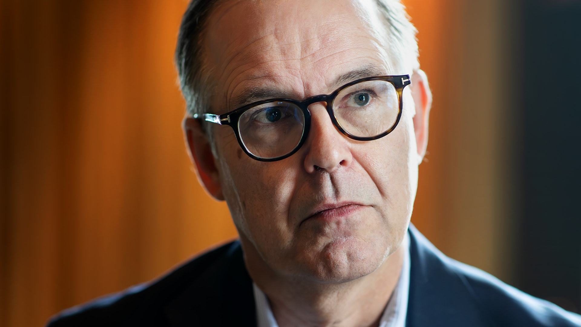 Porträttfoto av en man med glasögon mot en varm bakgrund.