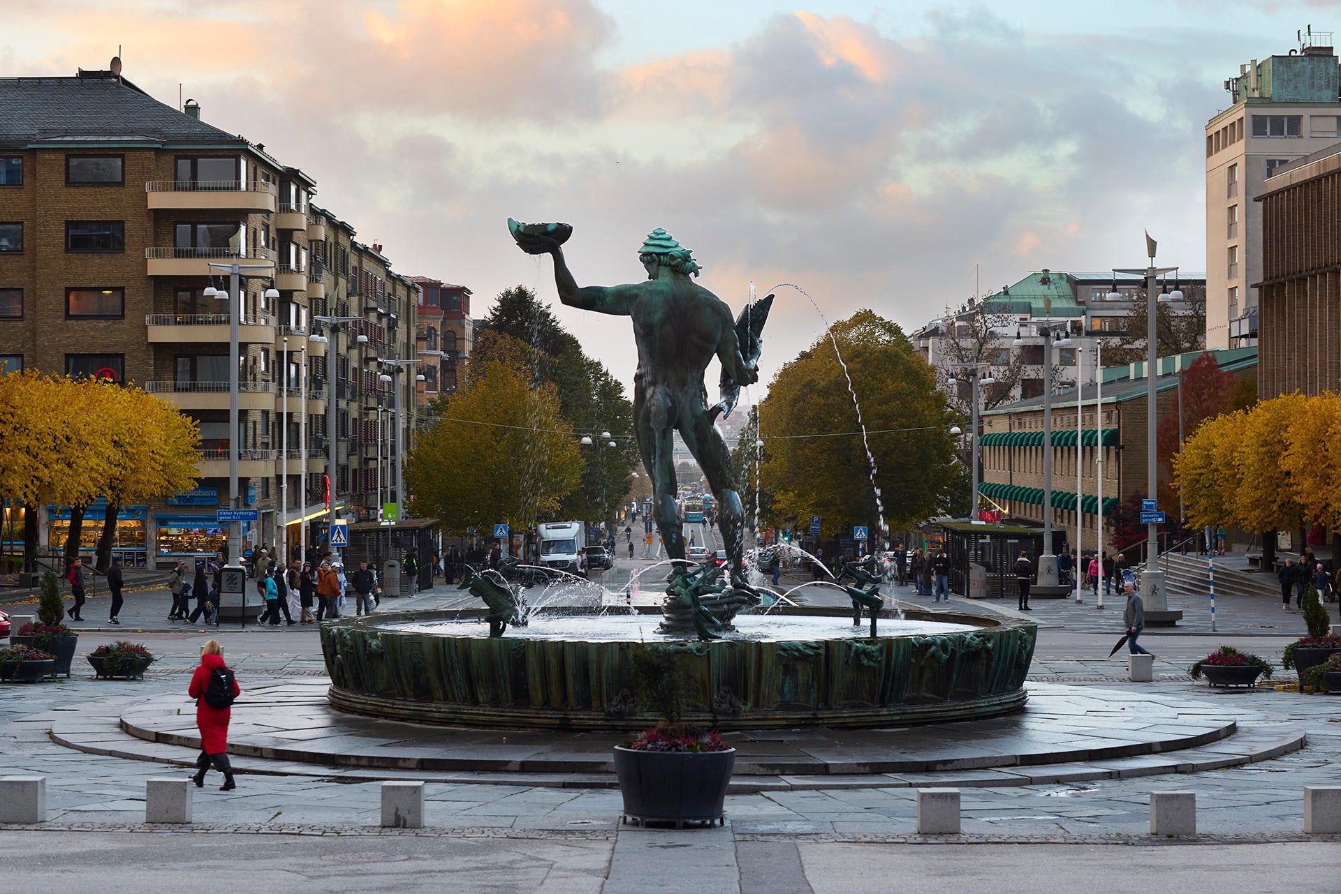 Statyn Poseidon på en fontän på Götaplatsen i Göteborg, omgiven av höstfärgade träd och byggnader.