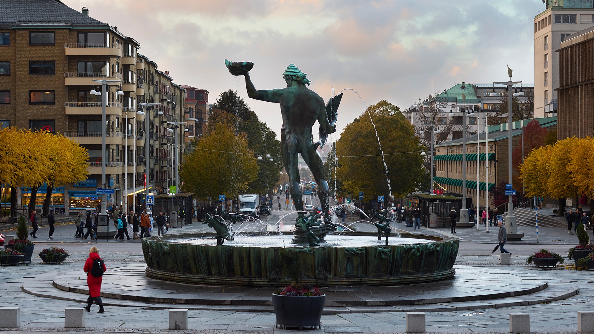 Statyn Poseidon på en fontän på Götaplatsen i Göteborg, omgiven av höstfärgade träd och byggnader.