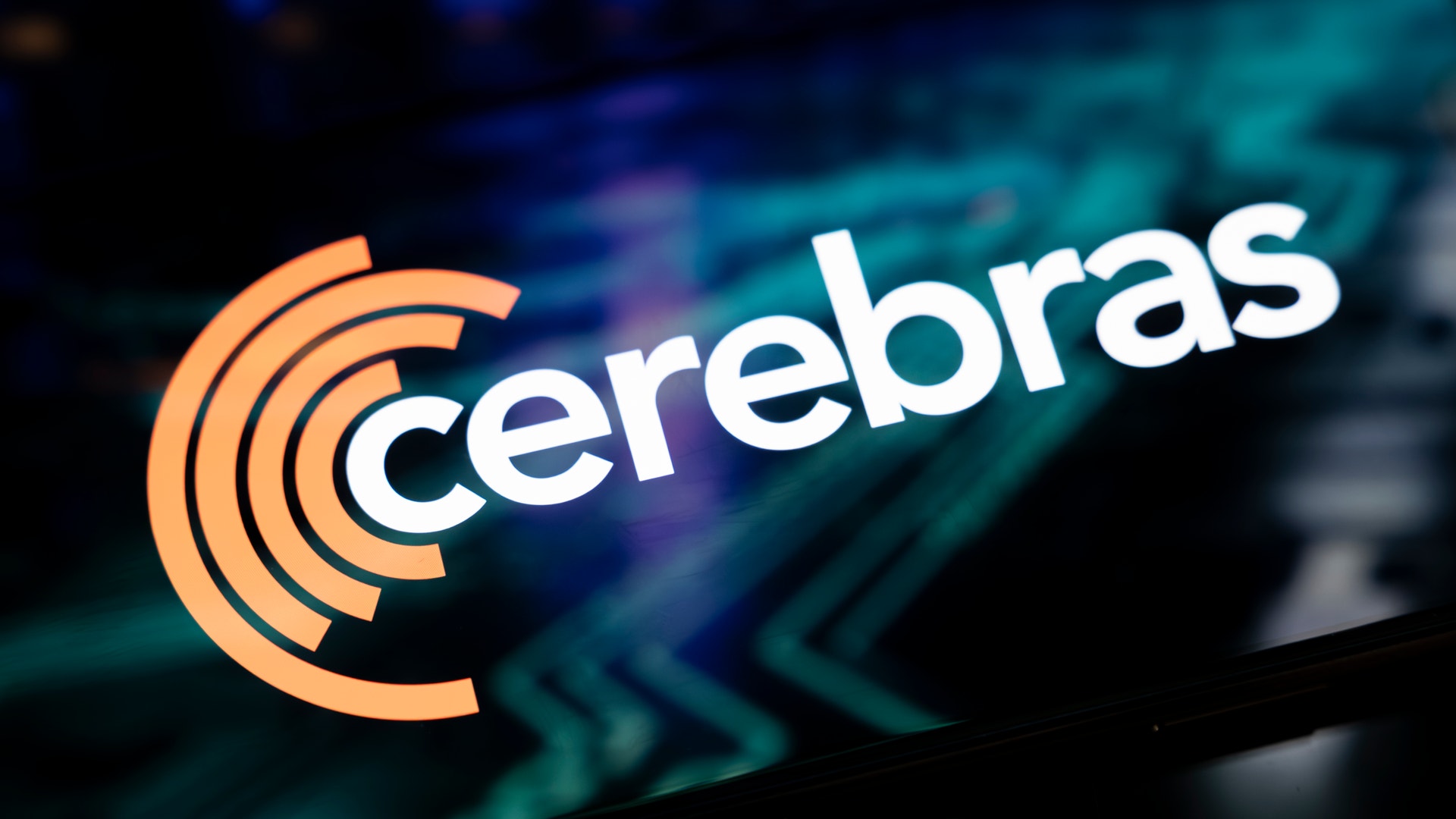 Cerebras-logotypen med orange koncentriska cirklar och vit text på en teknisk bakgrund med blå och gröna nyanser.