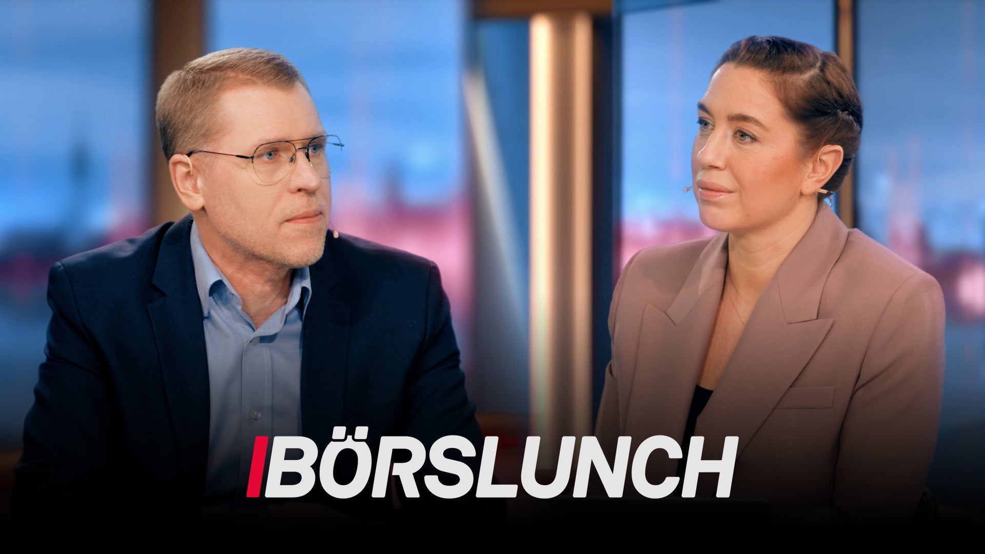 Två personer i diskussion i en TV-studio med stadsvy i bakgrunden. Programmet heter Börslunch.