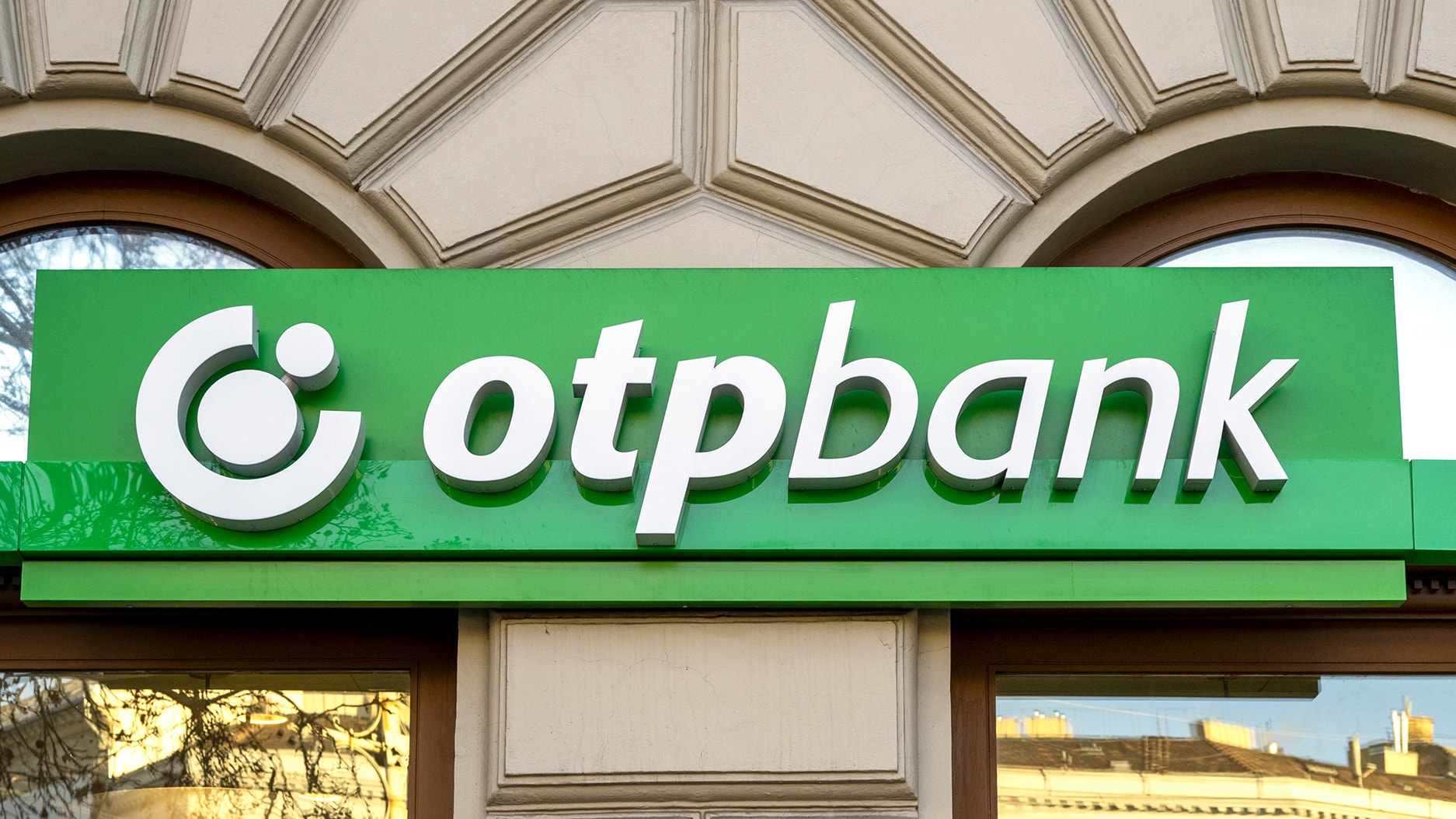 En grön skylt med texten "OTP Bank" på en byggnadsfasad.