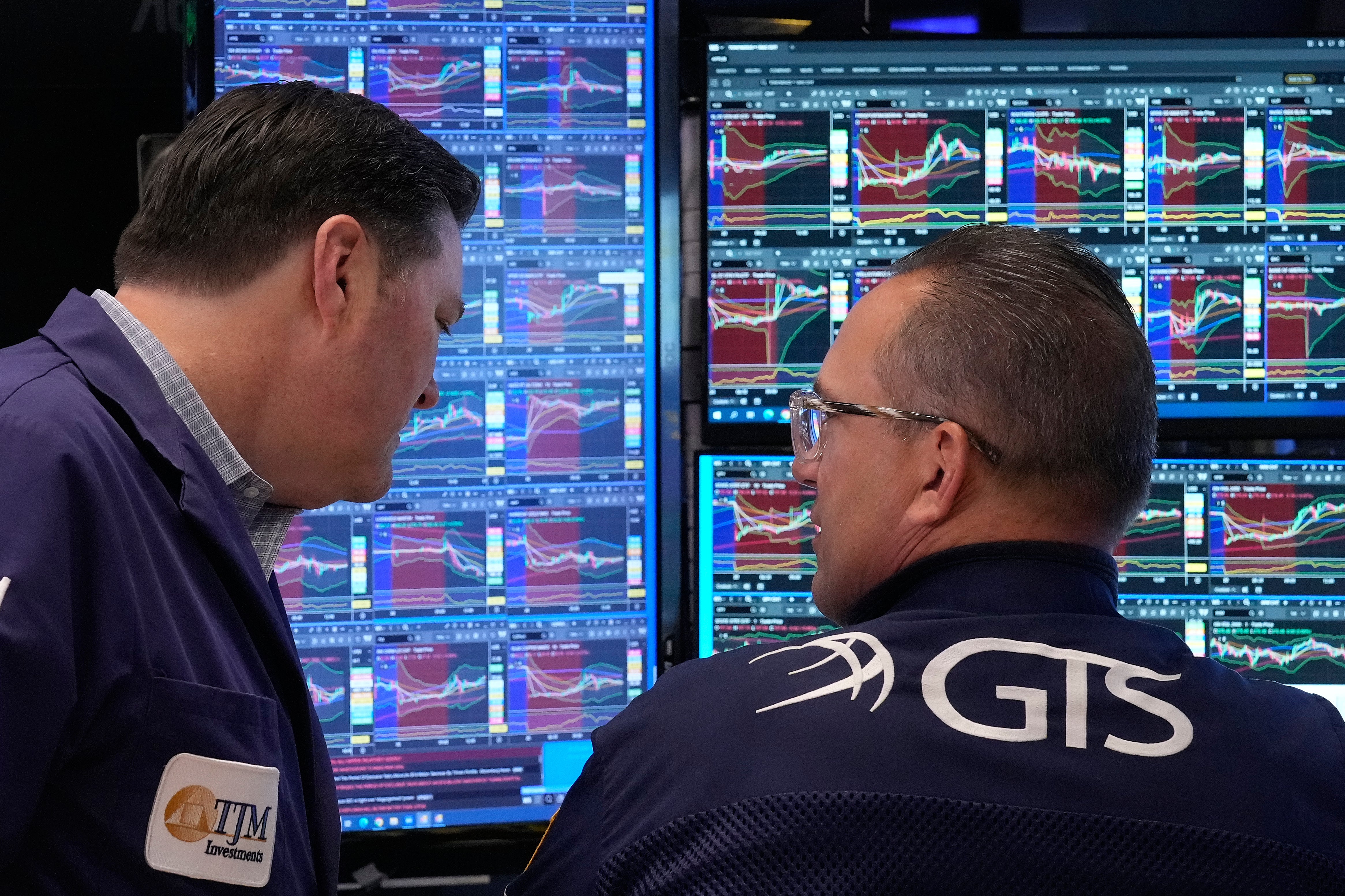 Två män tittar på finansiella handelsskärmar med grafer och marknadsdata.