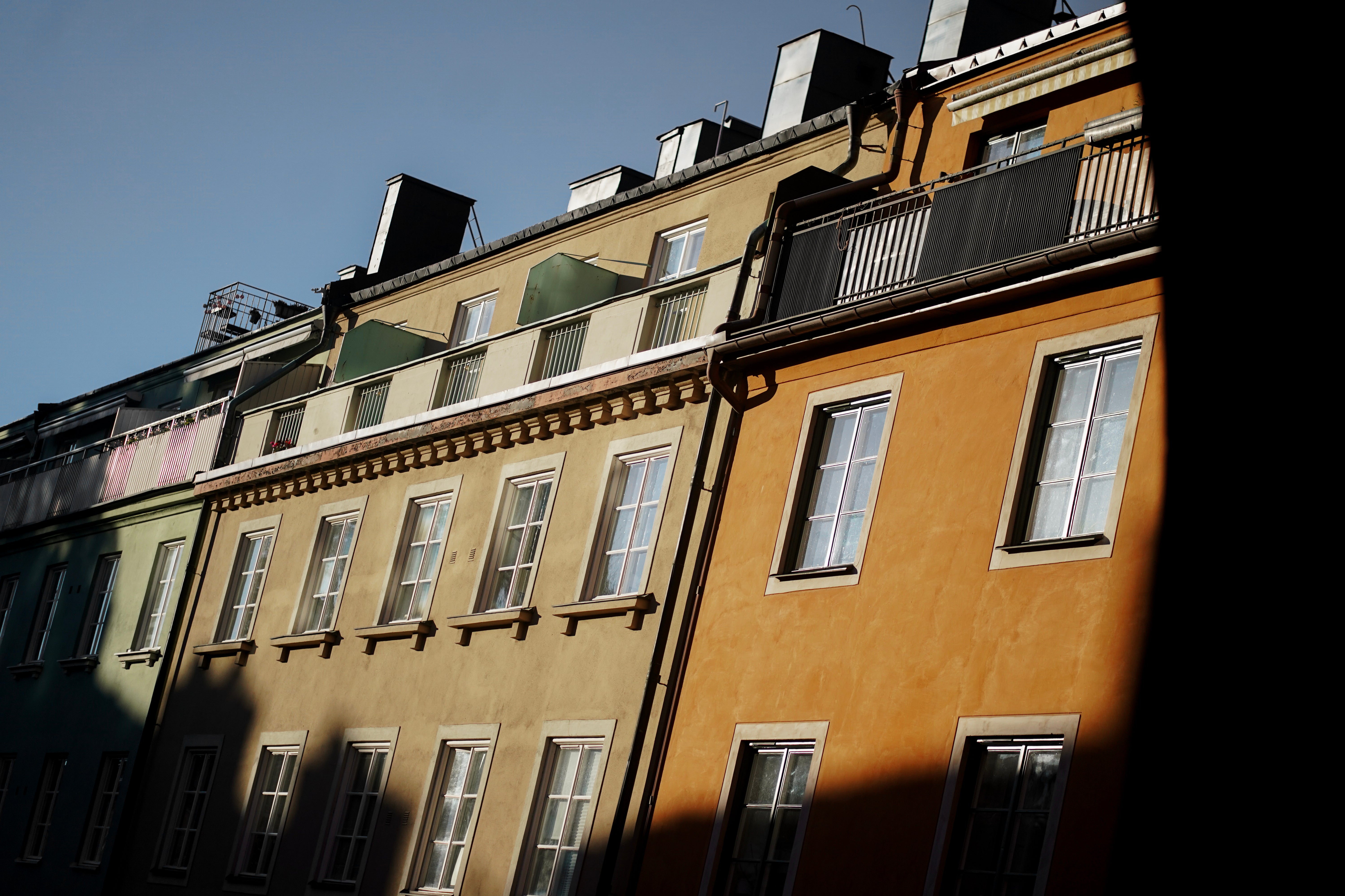 Rad av klassiska bostadshus med gula och beiga fasader, flera fönster och mansardtak mot blå himmel.