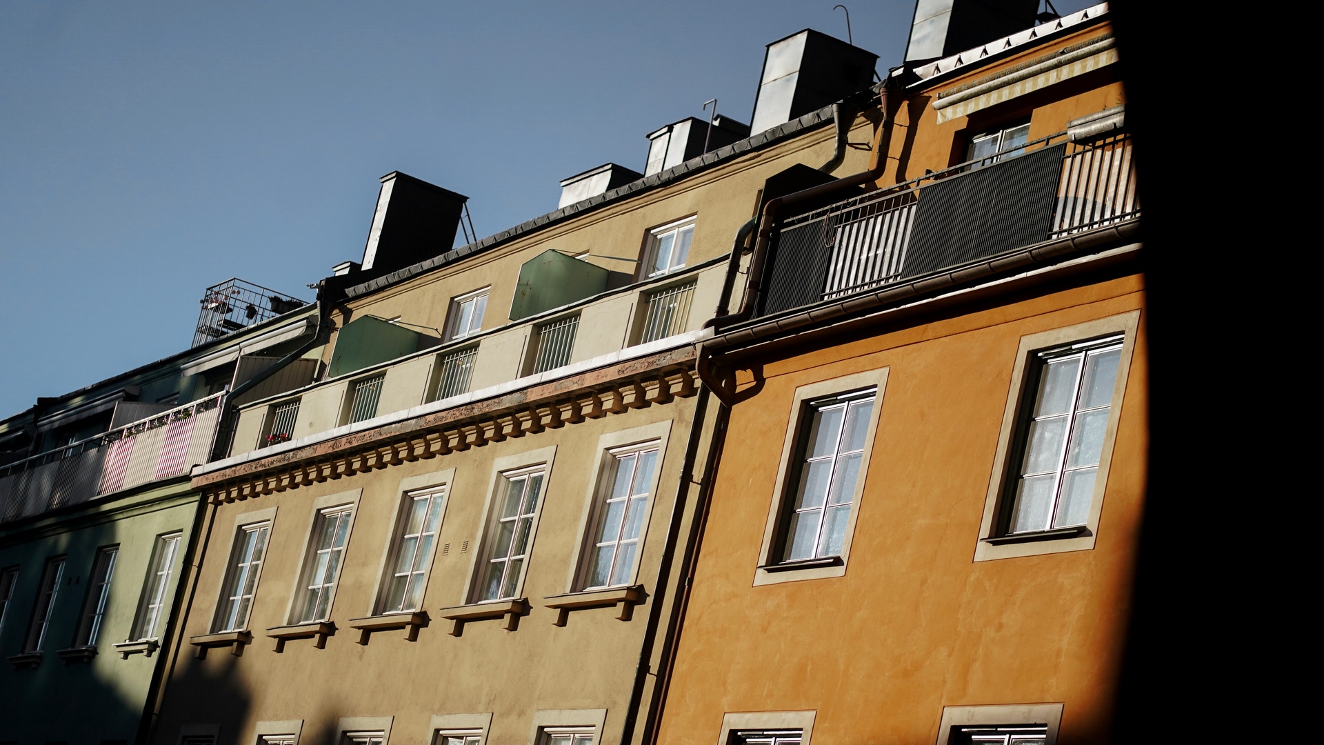 Rad av klassiska bostadshus med gula och beiga fasader, flera fönster och mansardtak mot blå himmel.