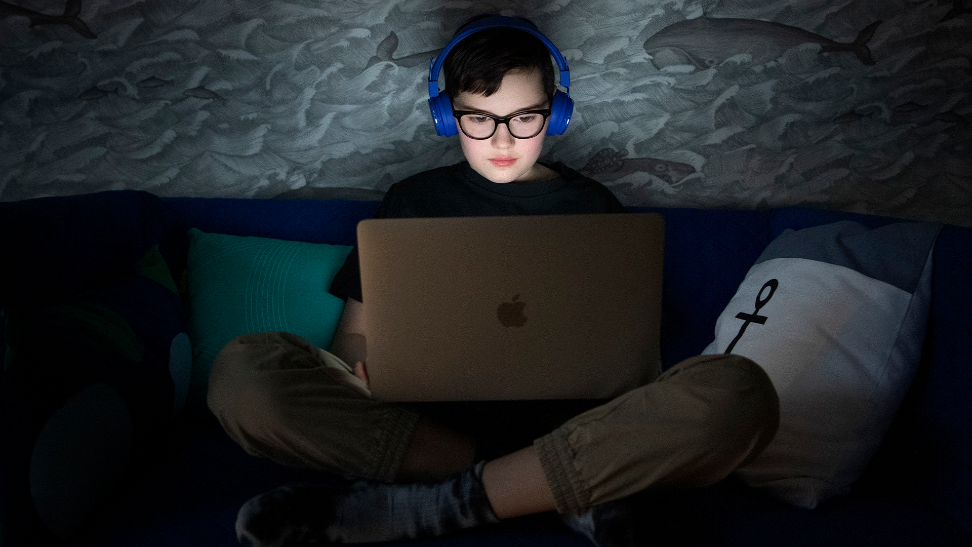 Ett barn sitter med hörlurar framför sin laptop. 