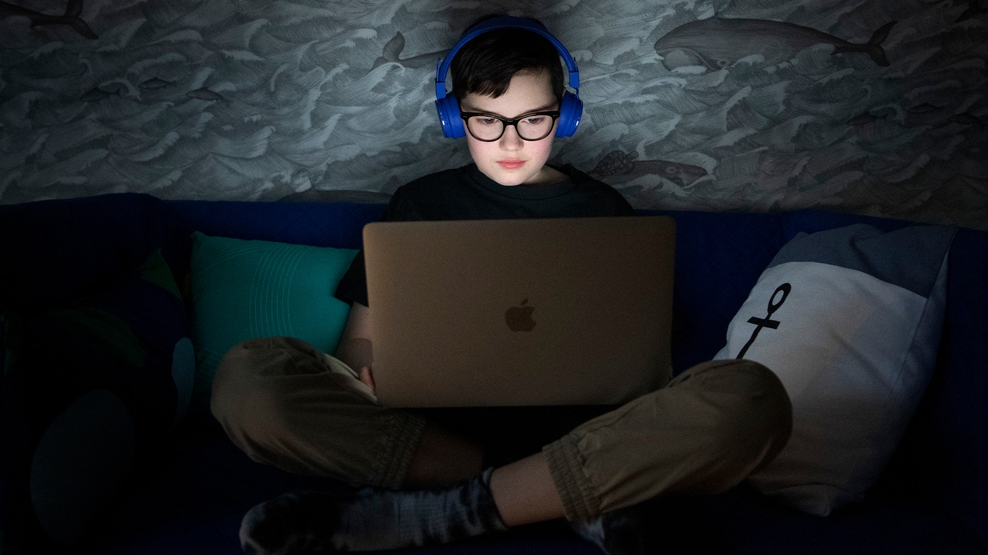 Ett barn sitter med hörlurar framför sin laptop.