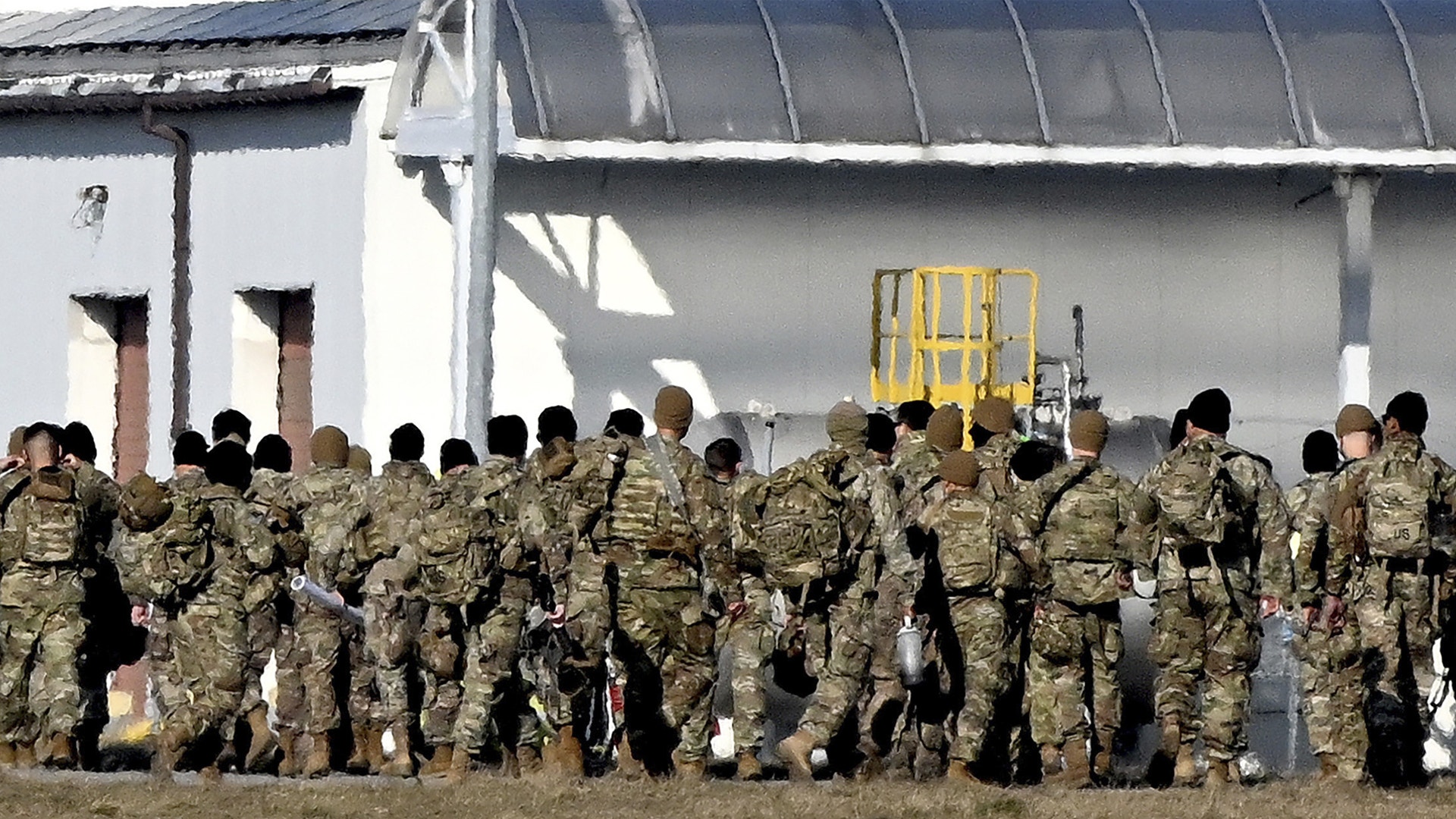 Grupp av militär personal i kamouflageuniformer samlade framför industribyggnader