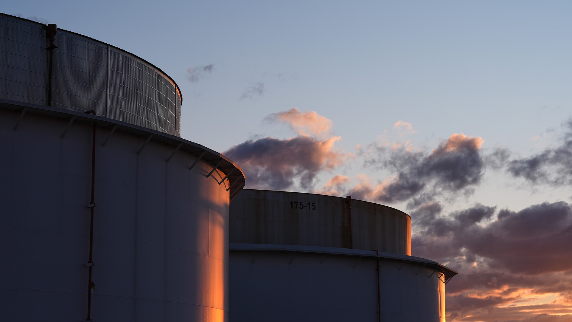 Stora industriella oljebehållare belysta av en dramatisk solnedgång