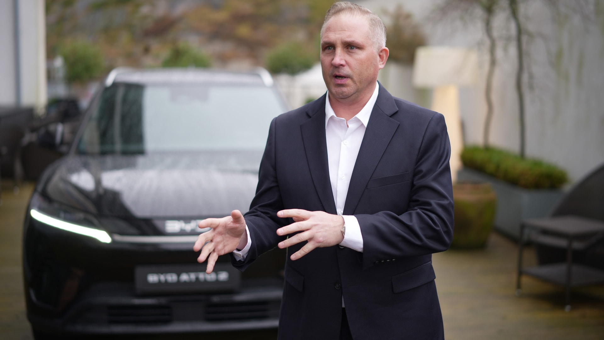 Man i kostym talar framför en elfordon