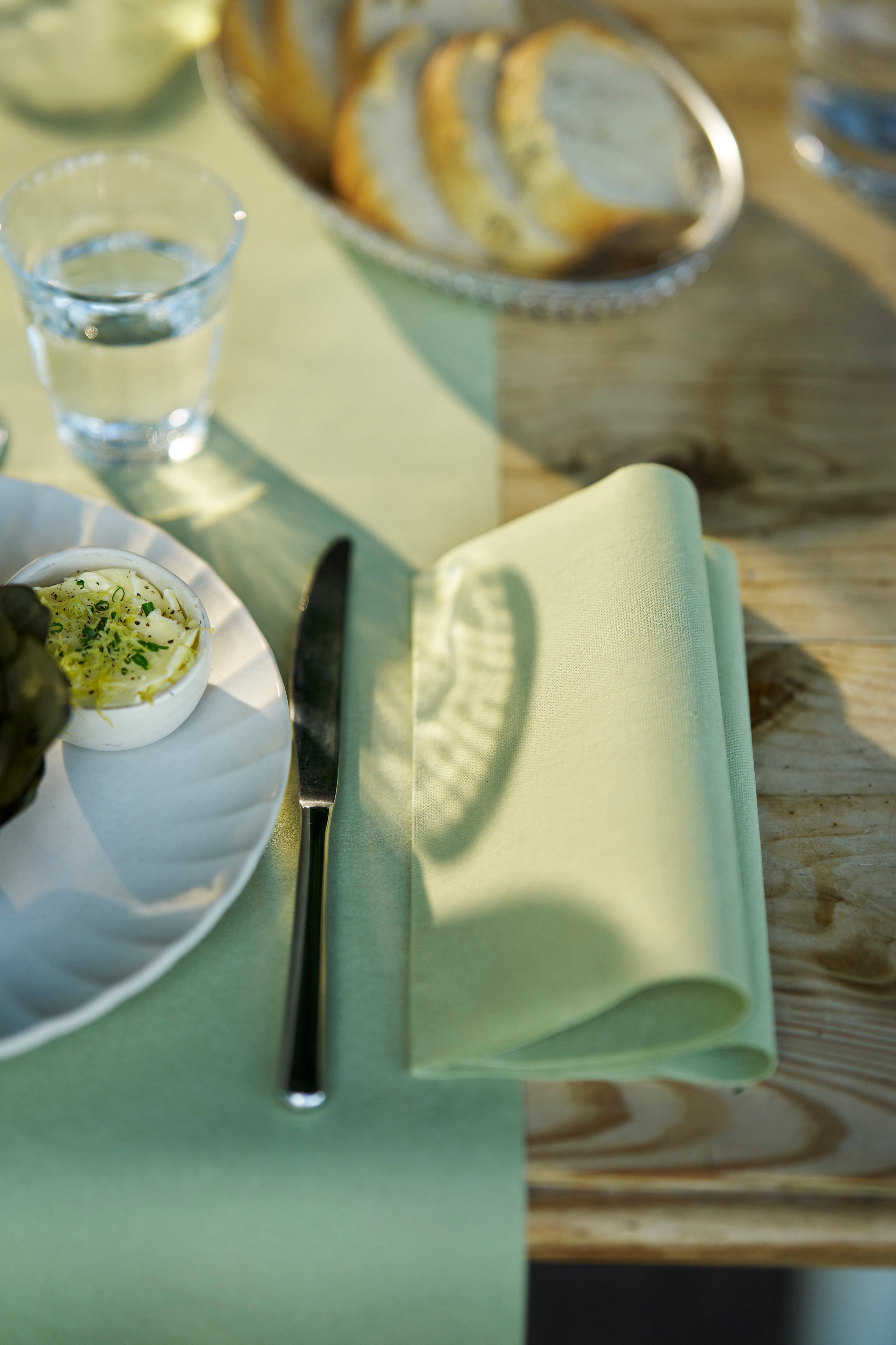 En bordsdukning med en pistaschgrön servett, vattenglas och tallrik med mat på ett trädgårdsbordet.