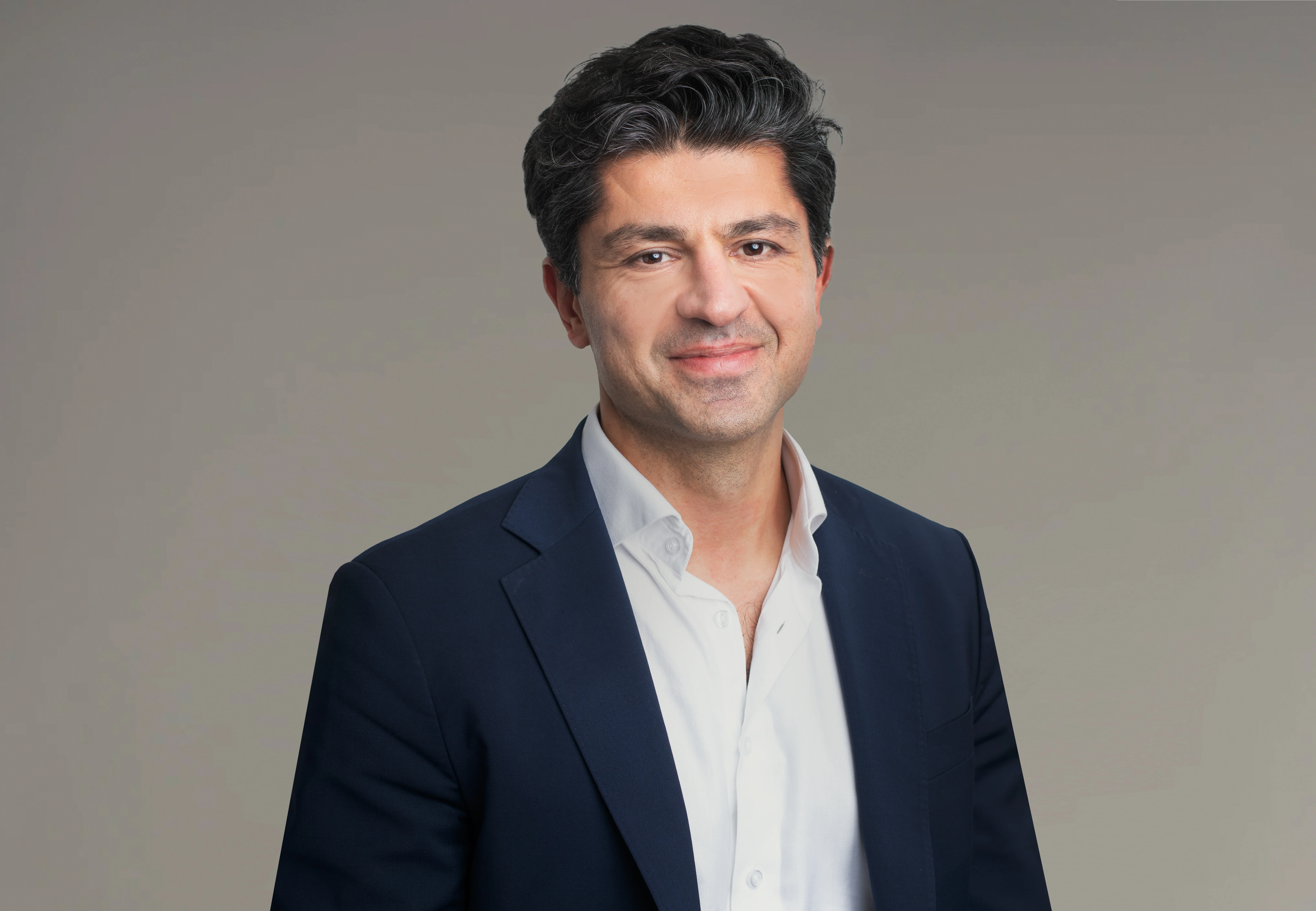 Porträttfoto av en man i mörkblå kavaj och vit skjorta mot neutral bakgrund.