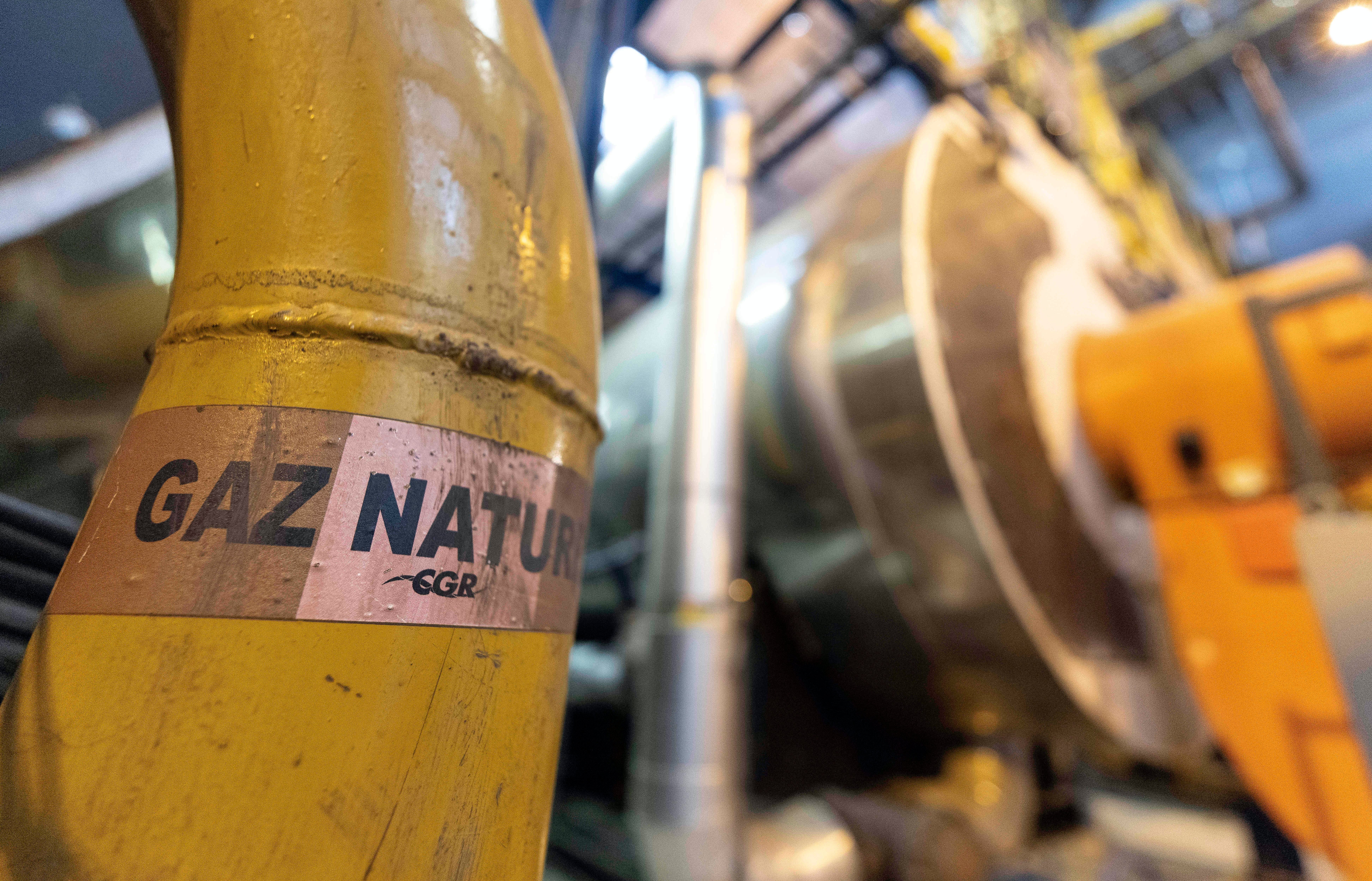 Närbild av en gul gaspipa märkt med etikett för naturgas, med industriell utrustning i bakgrunden.