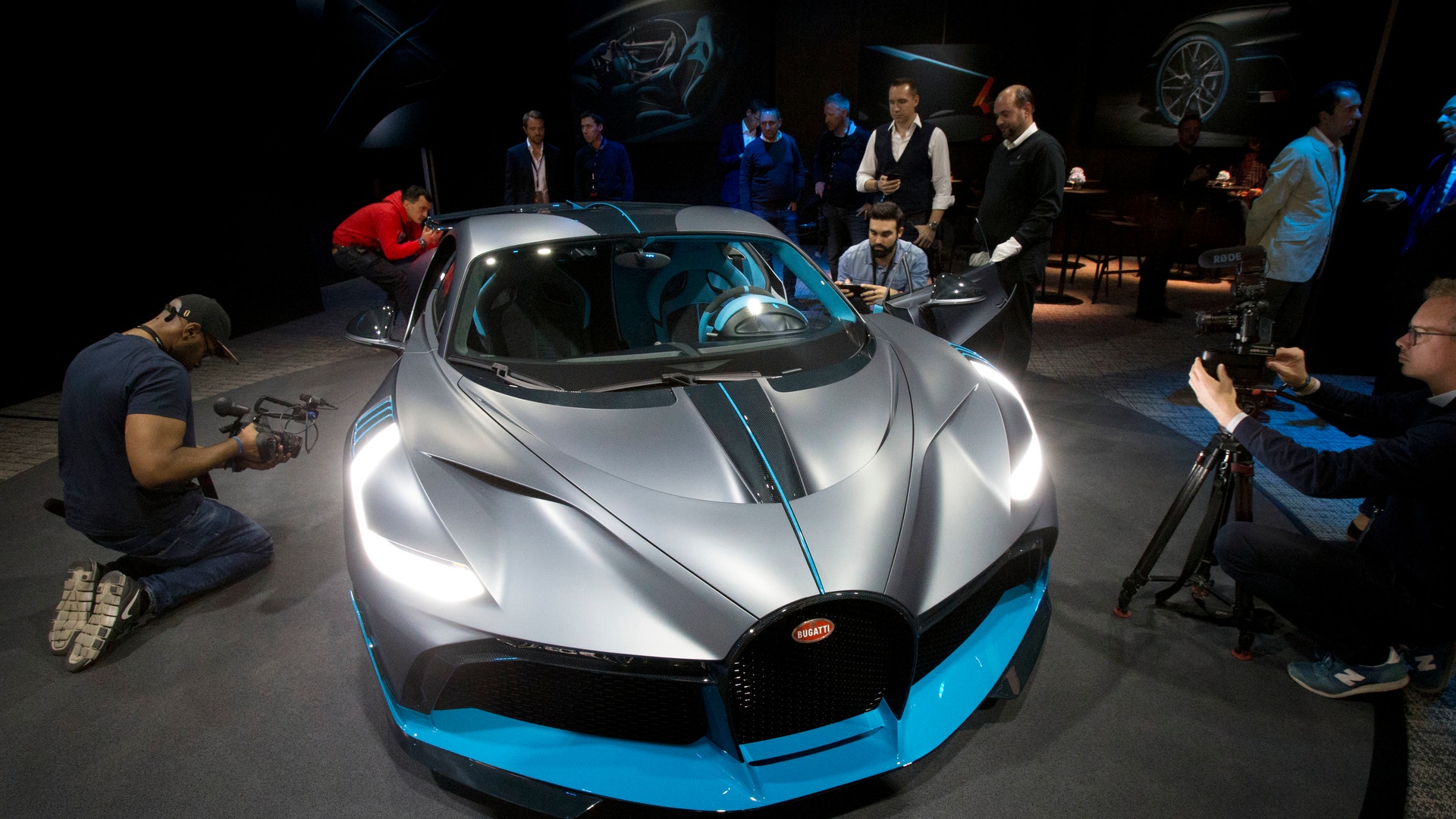 En silverfärgad och blå sportbil presenteras på en utställning med publik omkring.