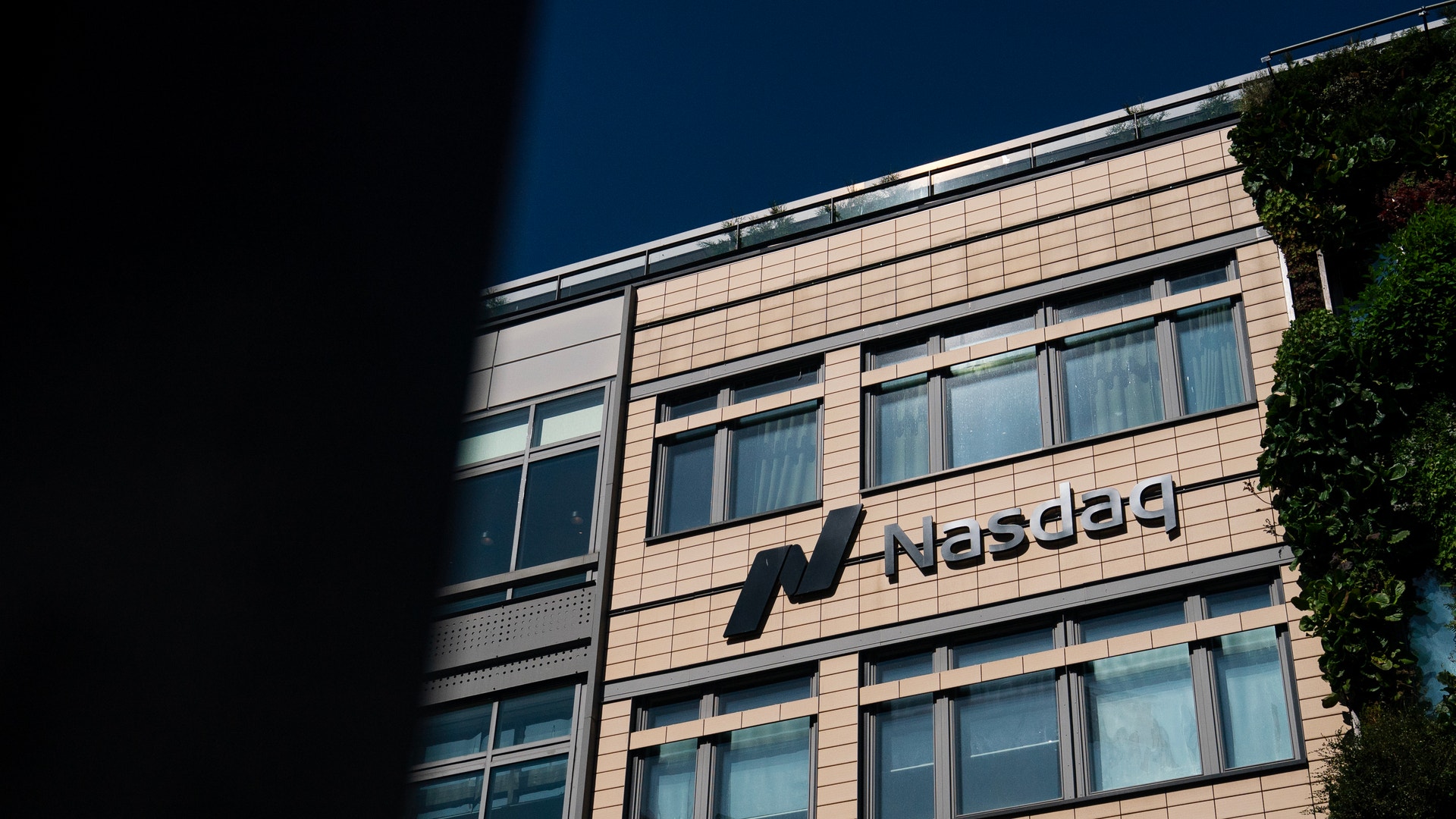 Fasad på en modern kontorsbyggnad med Nasdaq-logon. Byggnaden är klädd i ljus sten med många fönster.