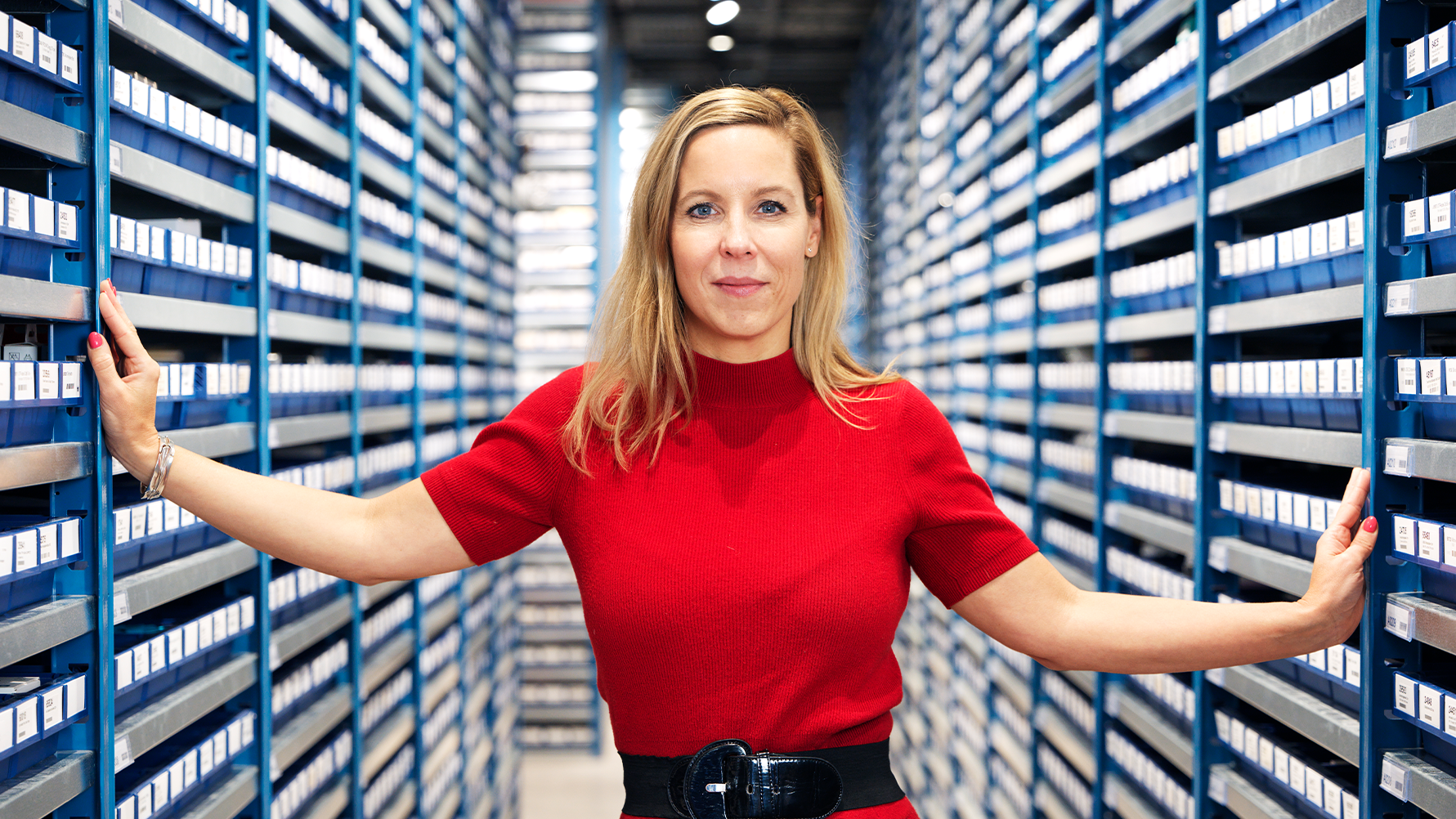 Kvinna i röd skjorta står mellan höga blå bokhyllor i ett bibliotek