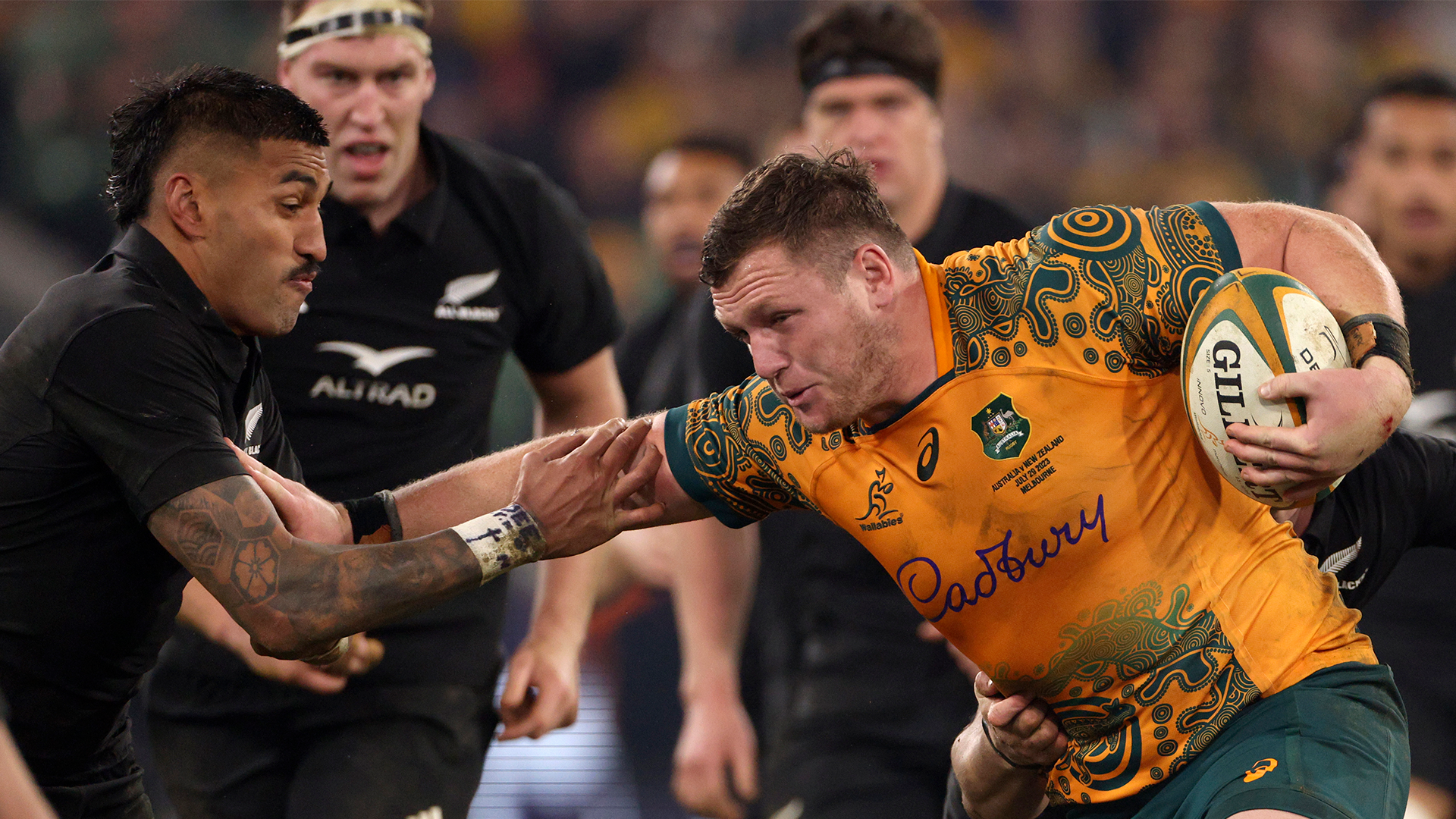 Rugbymatch mellan Australien och Nya Zeeland. En australiensisk spelare i gul och grön tröja med bollen försöker ta sig förbi en försvarare i svart.