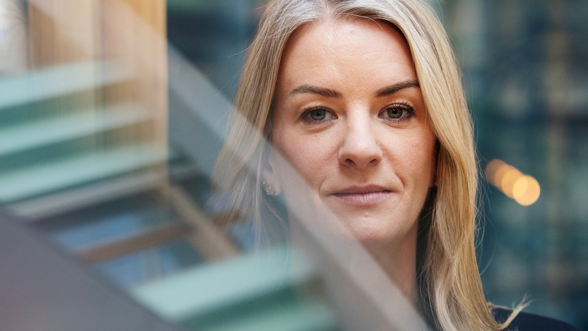 Porträtt av en kvinna med långt blont hår framför en stadsbyggnad