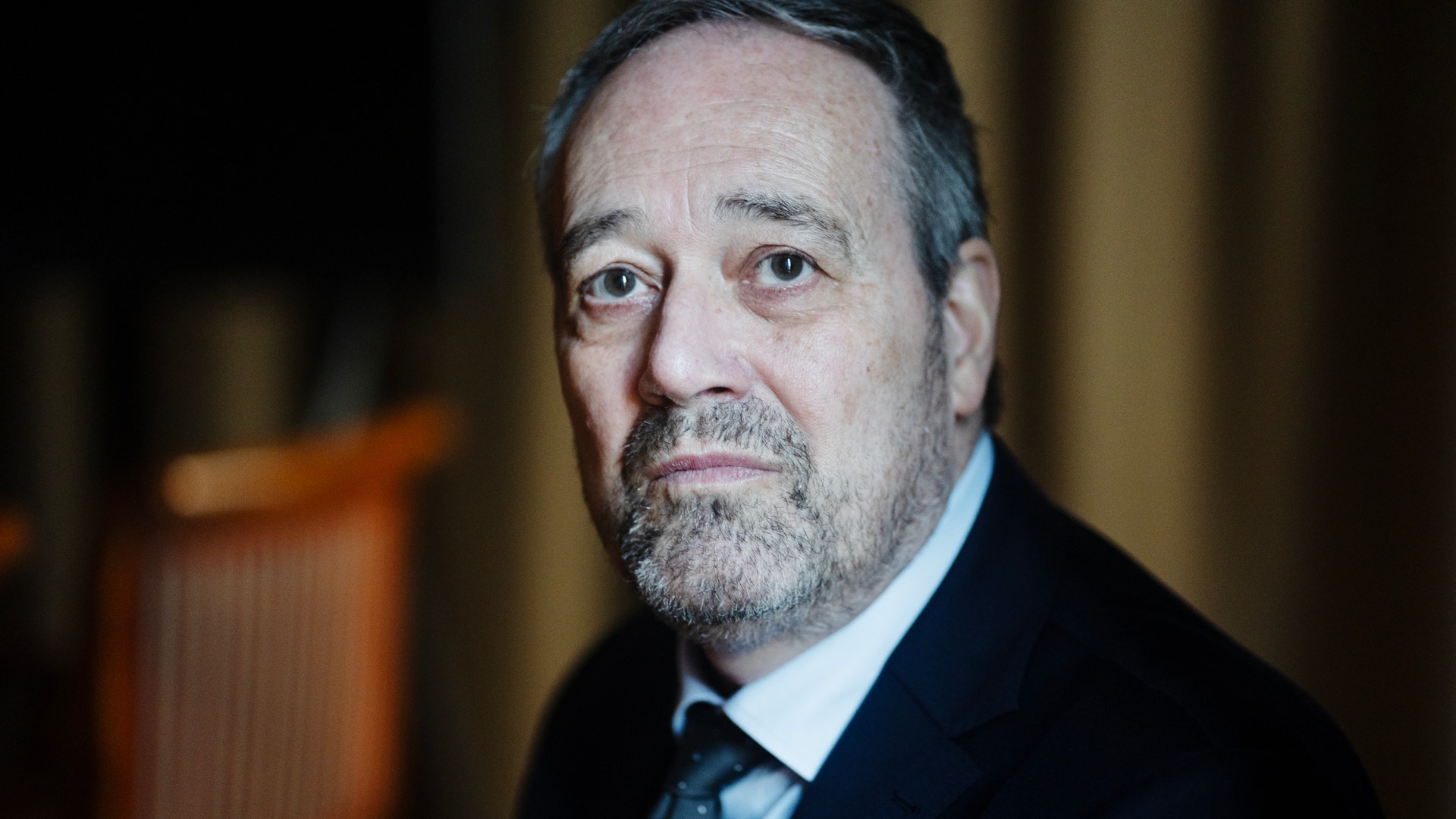 Porträttfoto av en man i kostym och slips mot en suddig bakgrund.