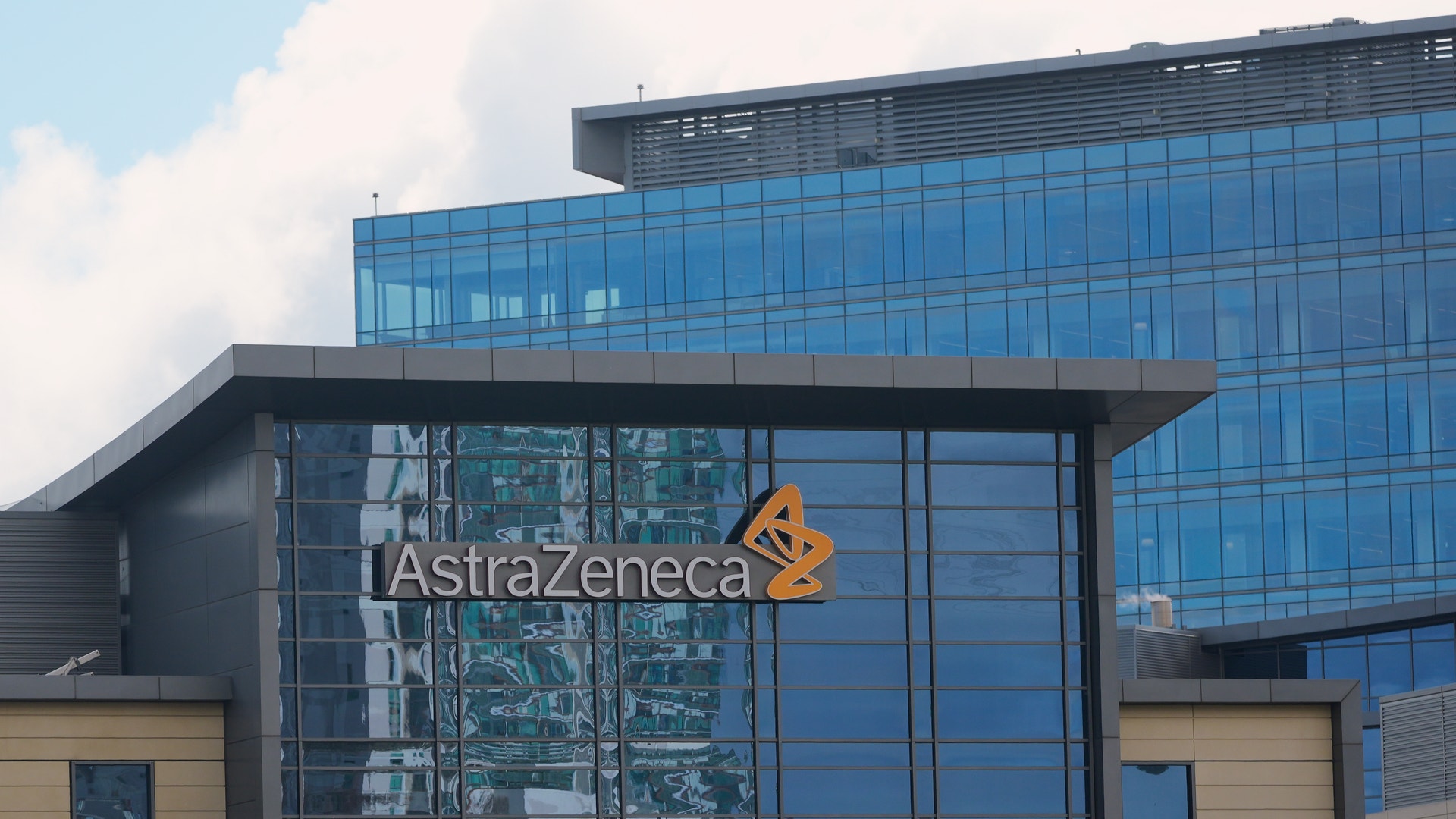 Modernt kontorsbyggnad med AstraZenecas logotyp och namn på fasaden. Byggnaden har stora glasfönster och blå färgschema.