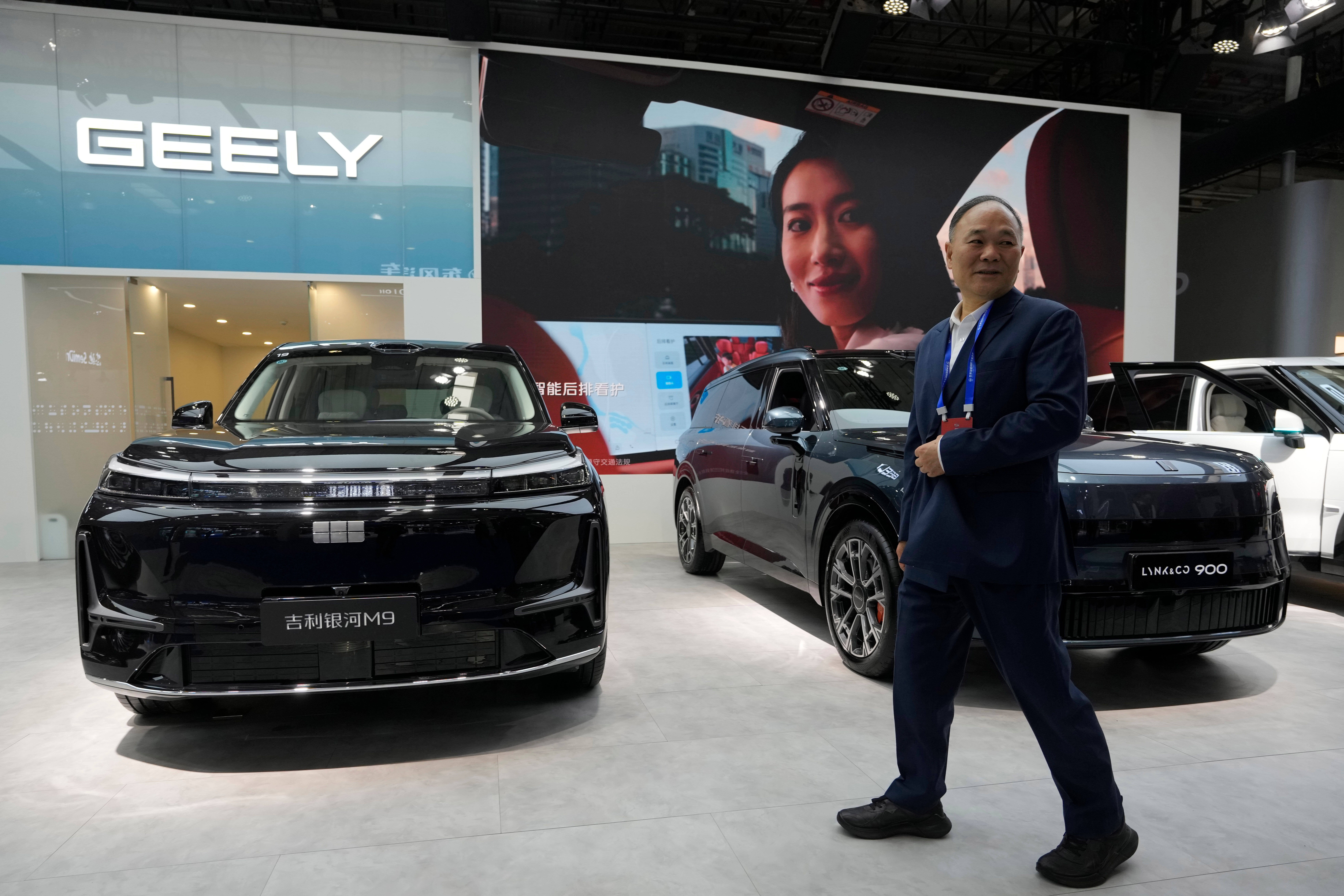Man i mörkblå kostym står framför svarta Geely-bilar på en bilutställning