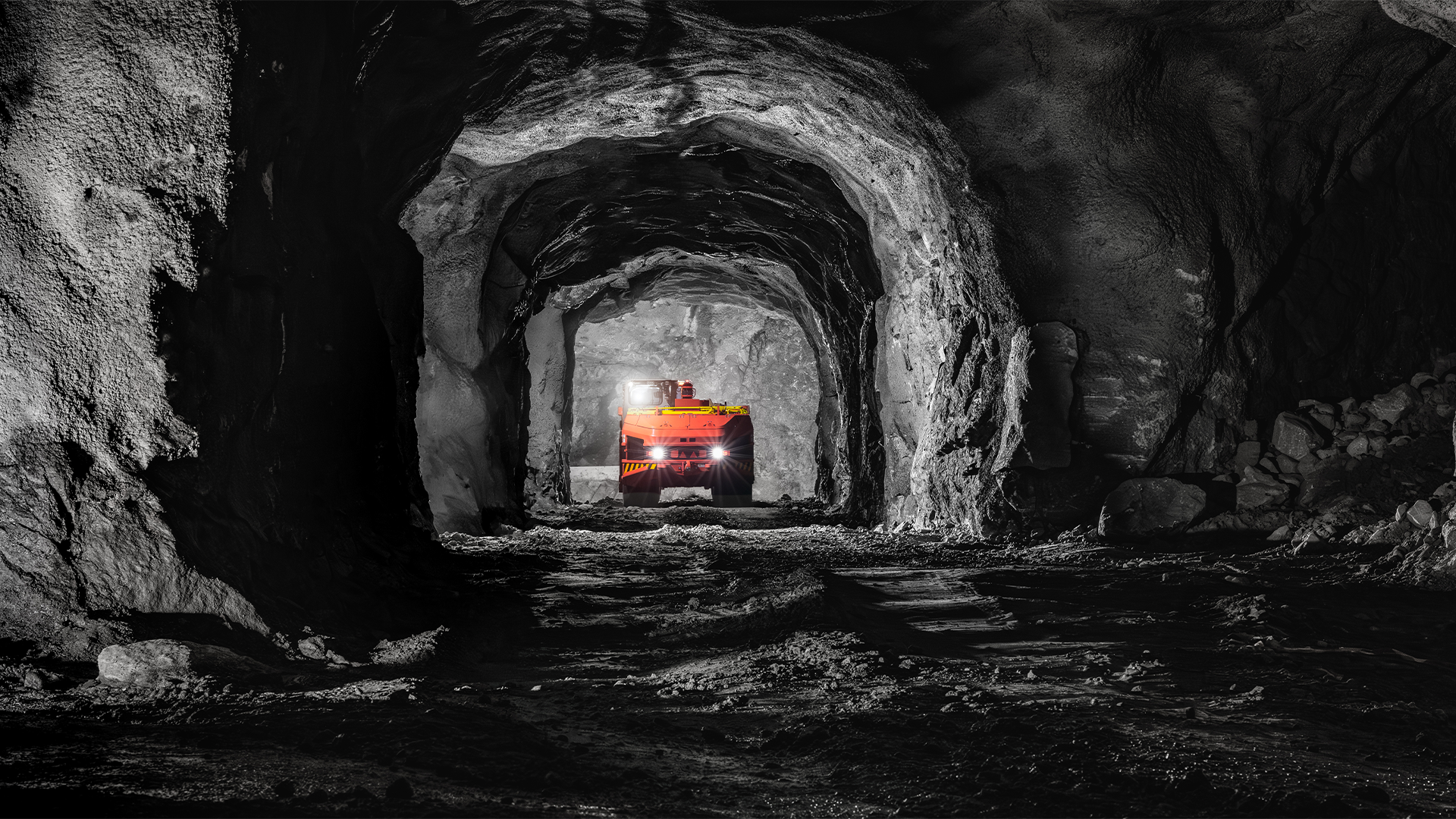 En orange gruvmaskin med tända strålkastare i en mörk gruvtunnel av berg.
