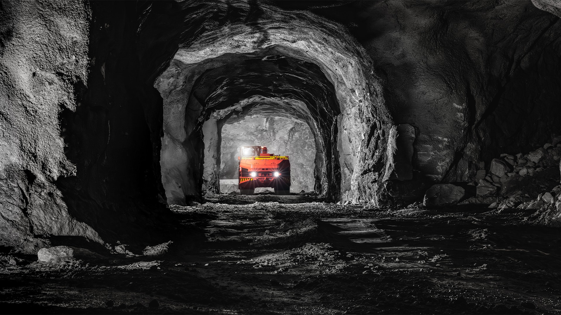 En orange gruvmaskin med tända strålkastare i en mörk gruvtunnel av berg.
