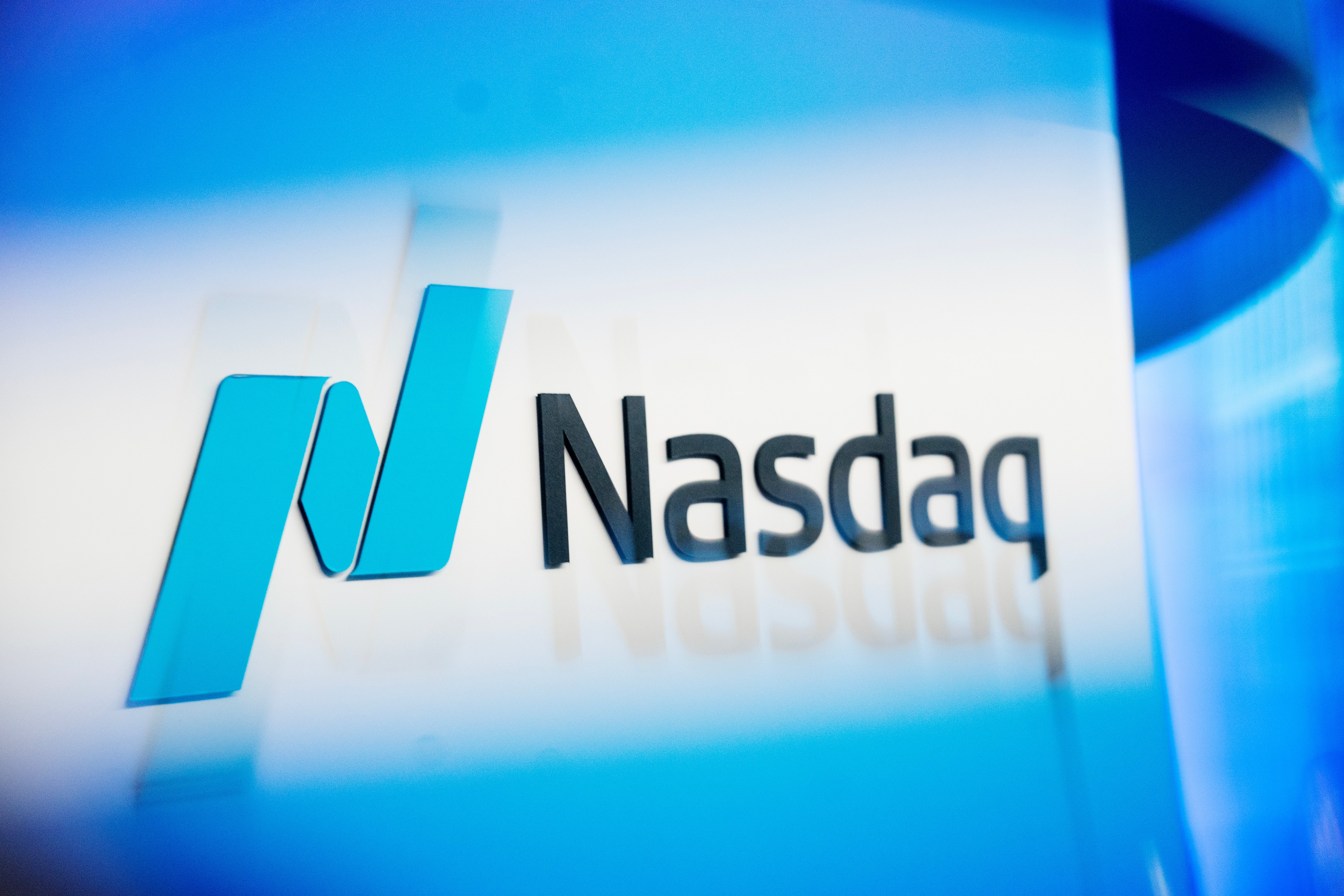 Nasdaqs logotyp i blått ljus mot en mörk bakgrund.