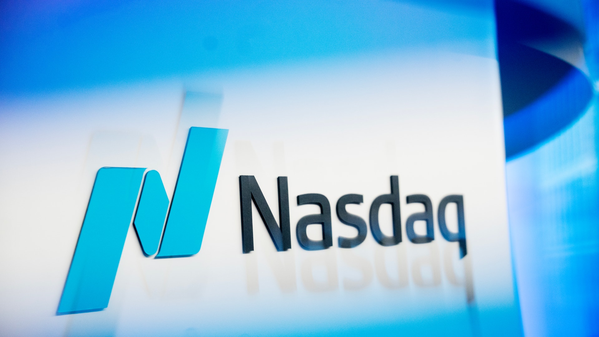 Nasdaqs logotyp i blått ljus mot en mörk bakgrund.
