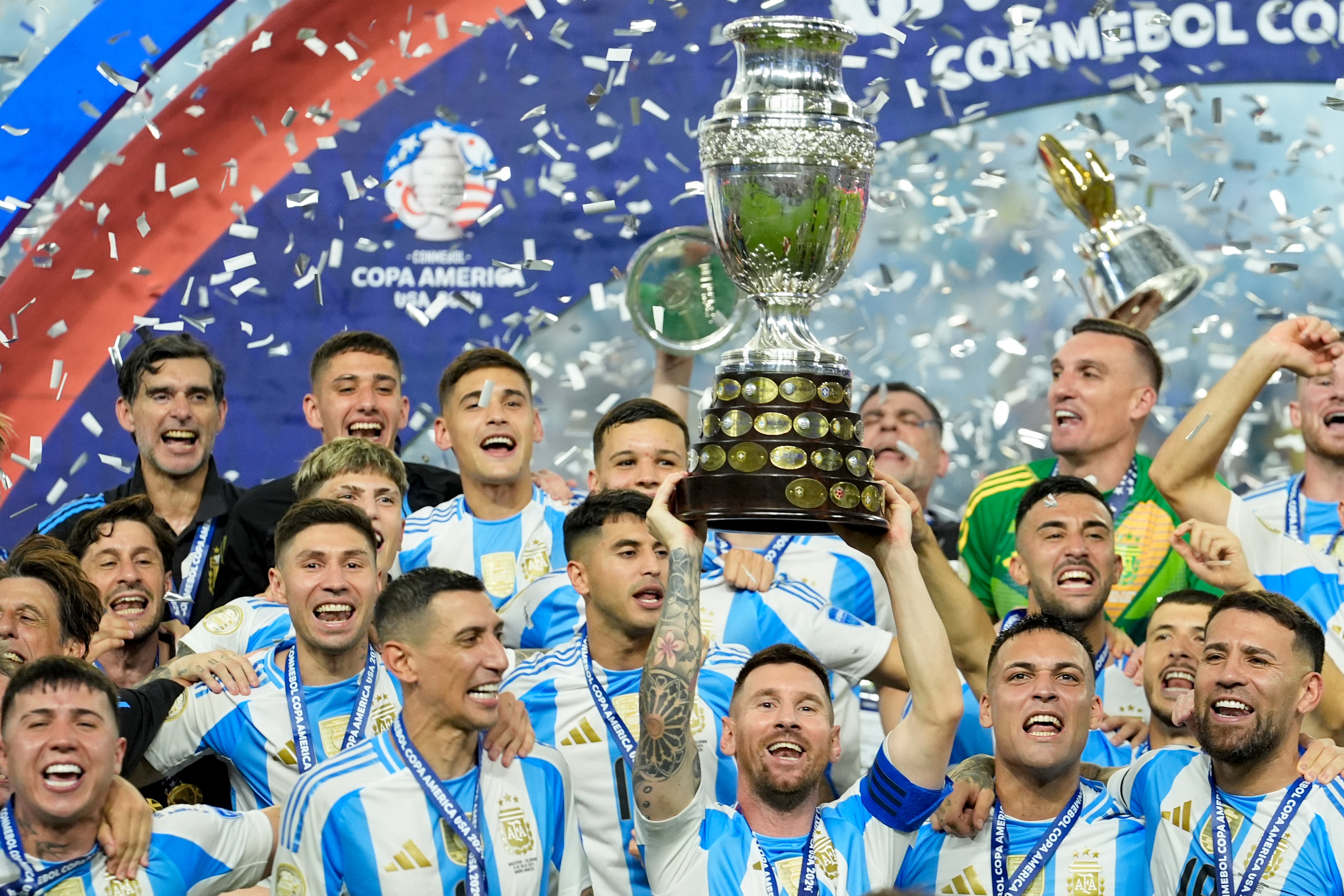 Fotbollslag i blå och vita randiga tröjor firar med en stor pokal medan konfetti regnar ner. Copa América-logon syns i bakgrunden.