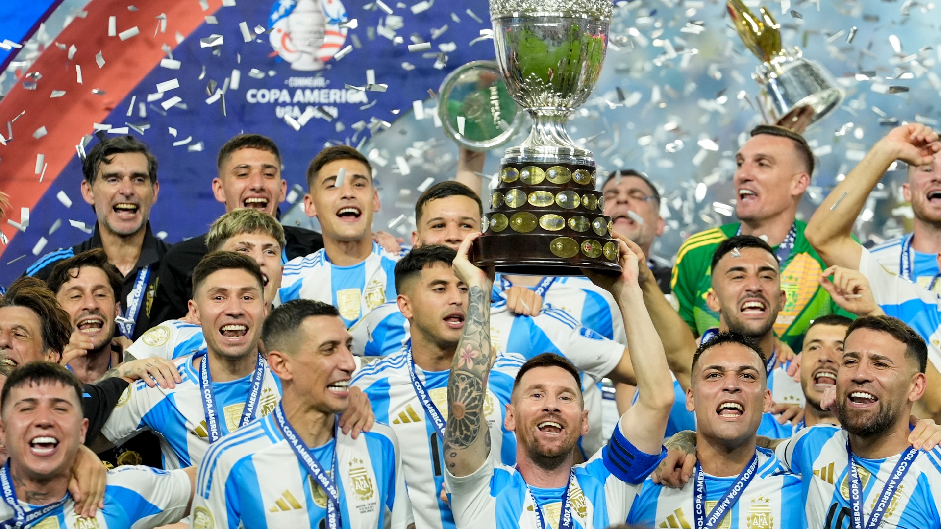 Fotbollslag i blå och vita randiga tröjor firar med en stor pokal medan konfetti regnar ner. Copa América-logon syns i bakgrunden.