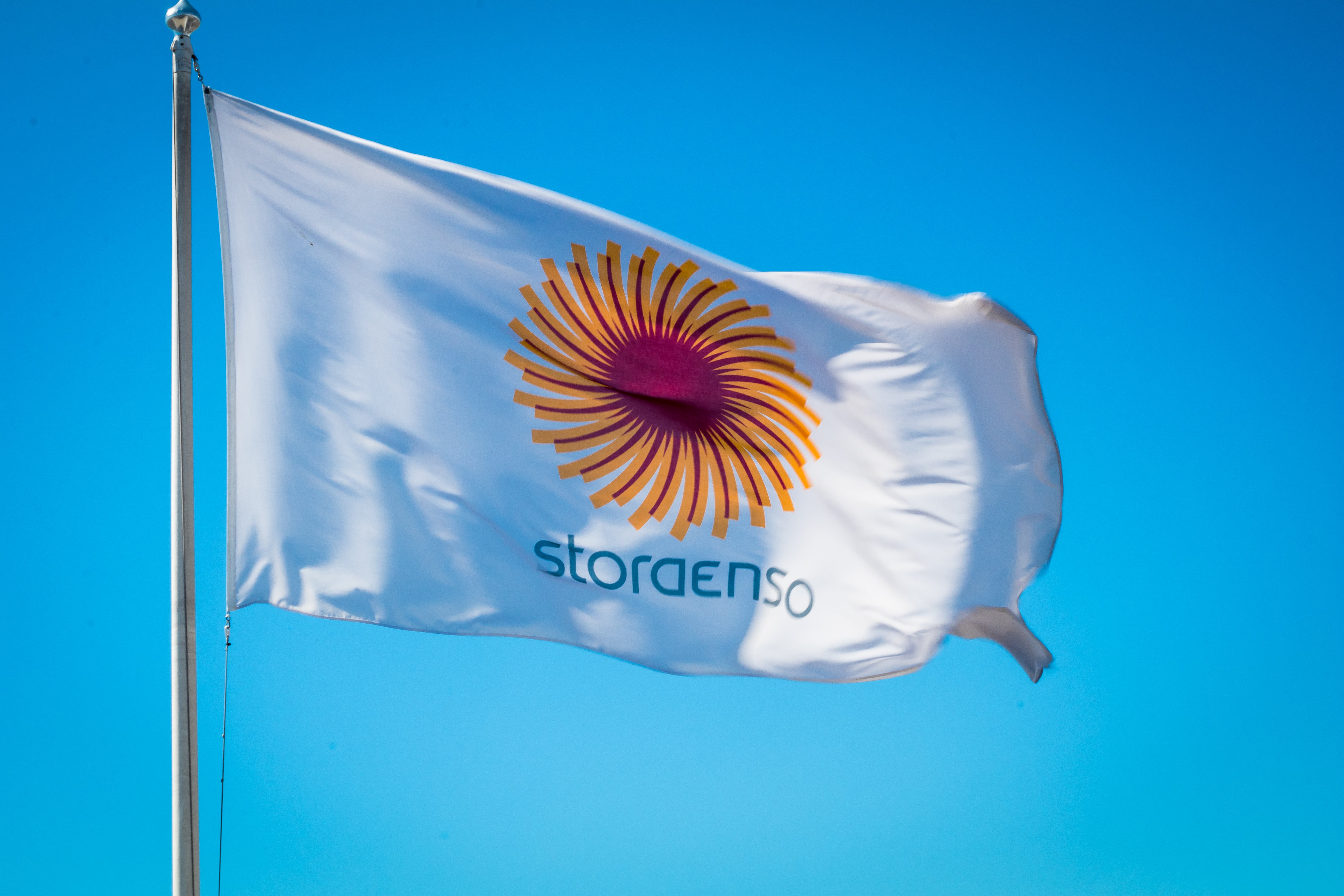 Stora Ensos flagga med orange solformad logotyp vajar mot blå himmel