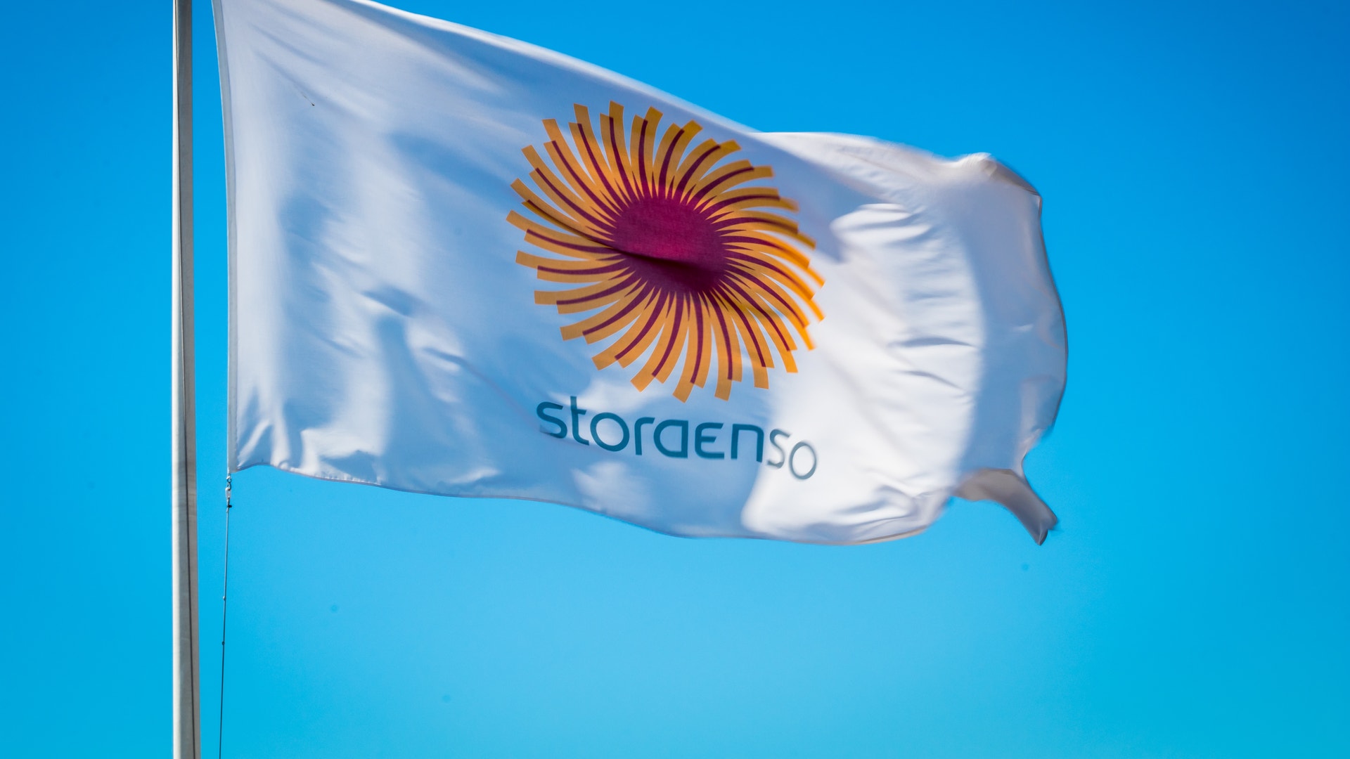 Stora Ensos flagga med orange solformad logotyp vajar mot blå himmel