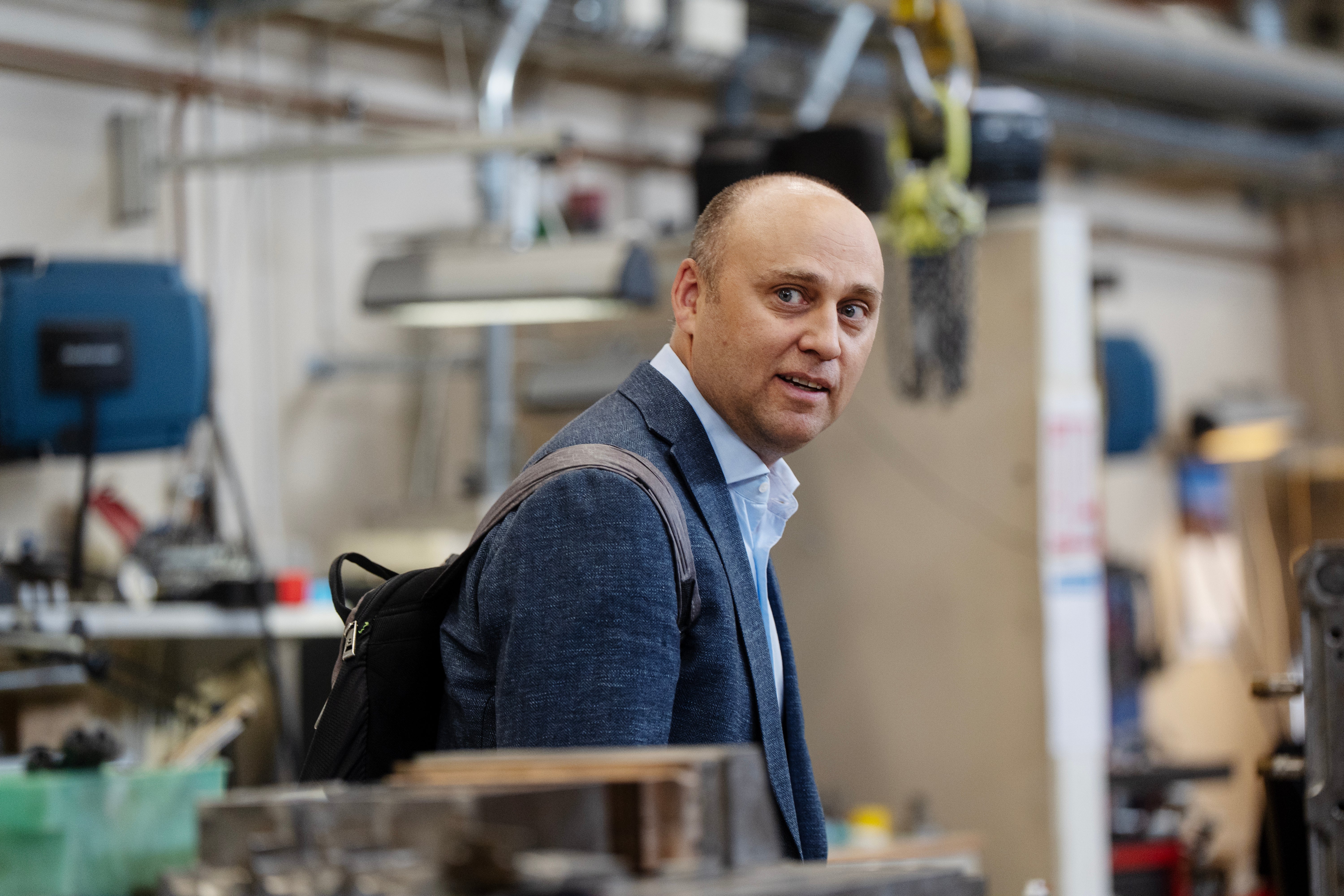 En man i mörkblå kavaj och ljusblå skjorta står i en fabrik och ser över axeln mot kameran.