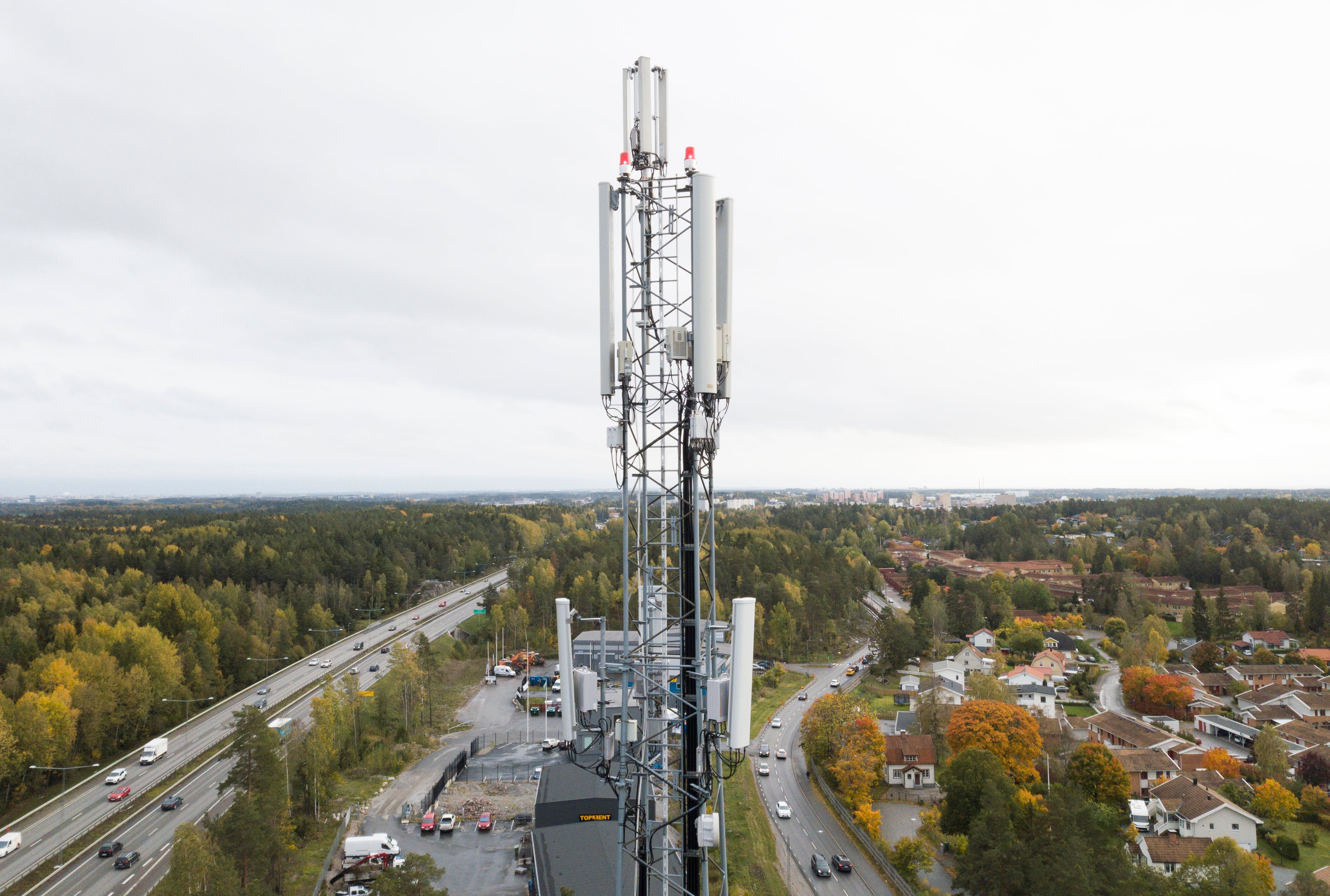 Luftfoto av en mobilmast som står på en plattform omgiven av skog och bostäder.