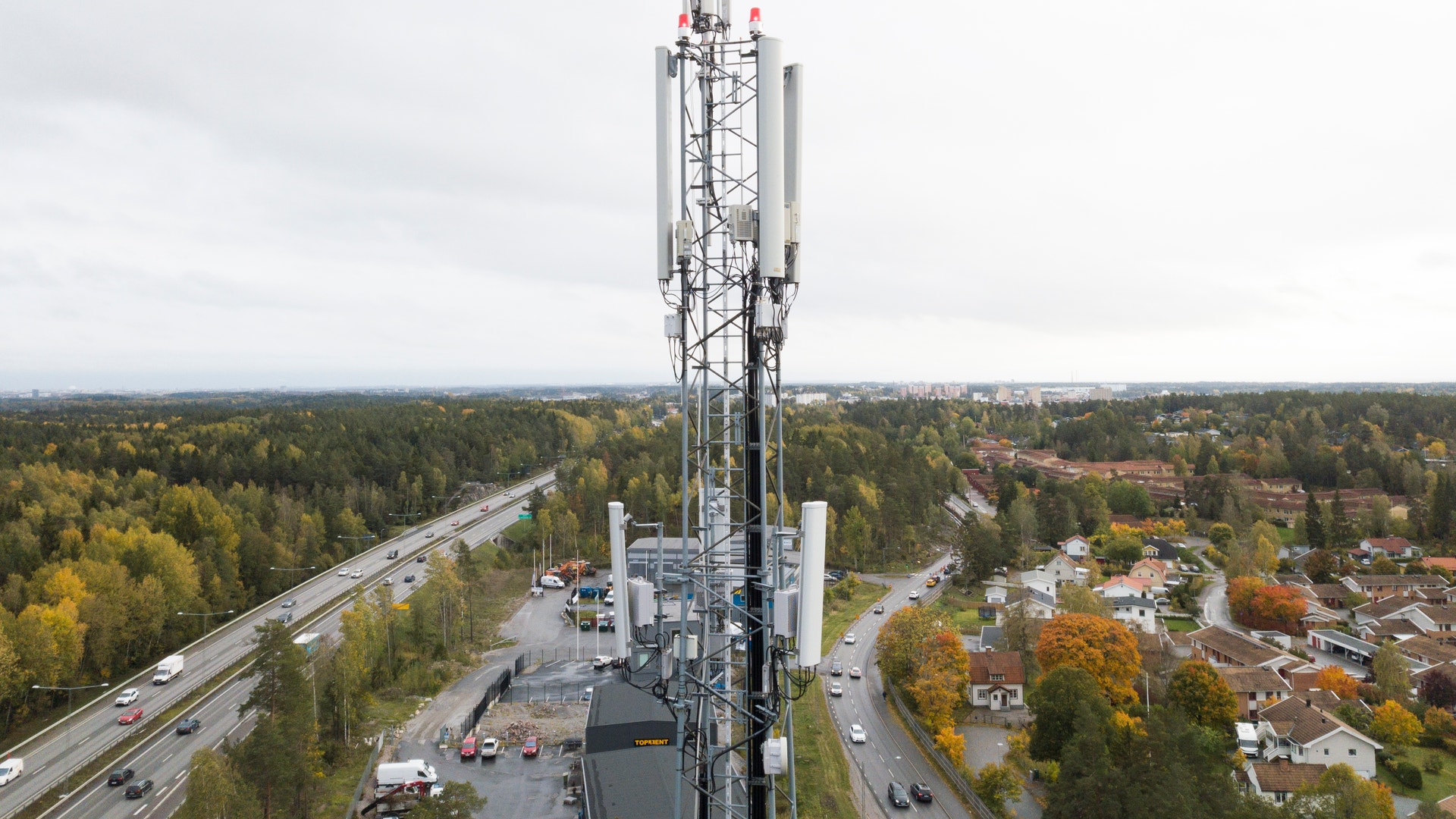 Luftfoto av en mobilmast som står på en plattform omgiven av skog och bostäder.