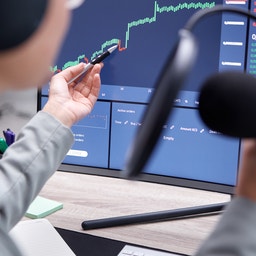 Person pekar på en datorskärm med finansiella grafer och marknadsdata medan den håller en datormus.