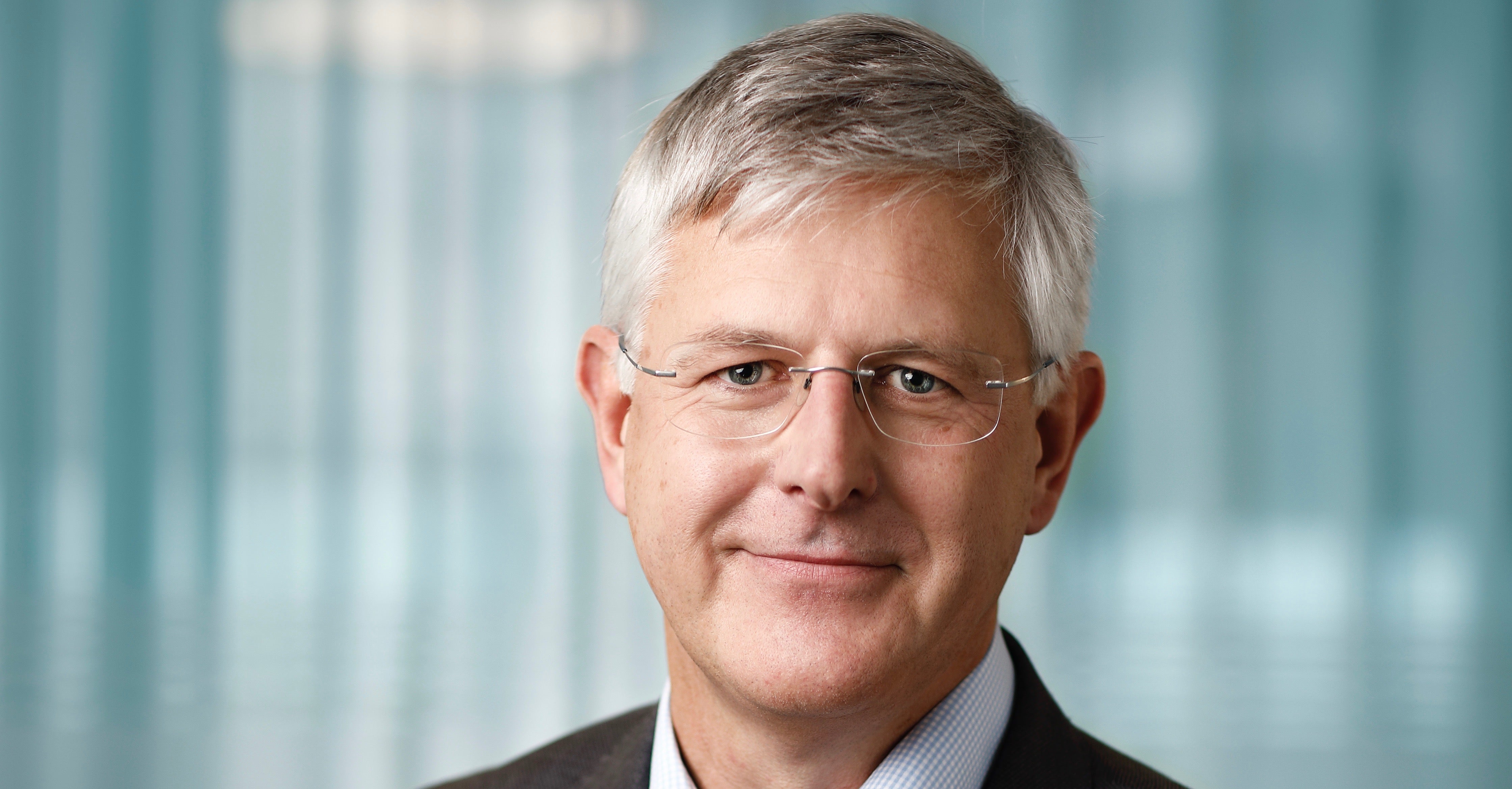 Porträttfoto av en man i affärskläder med glasögon mot en suddig kontorsbakgrund.