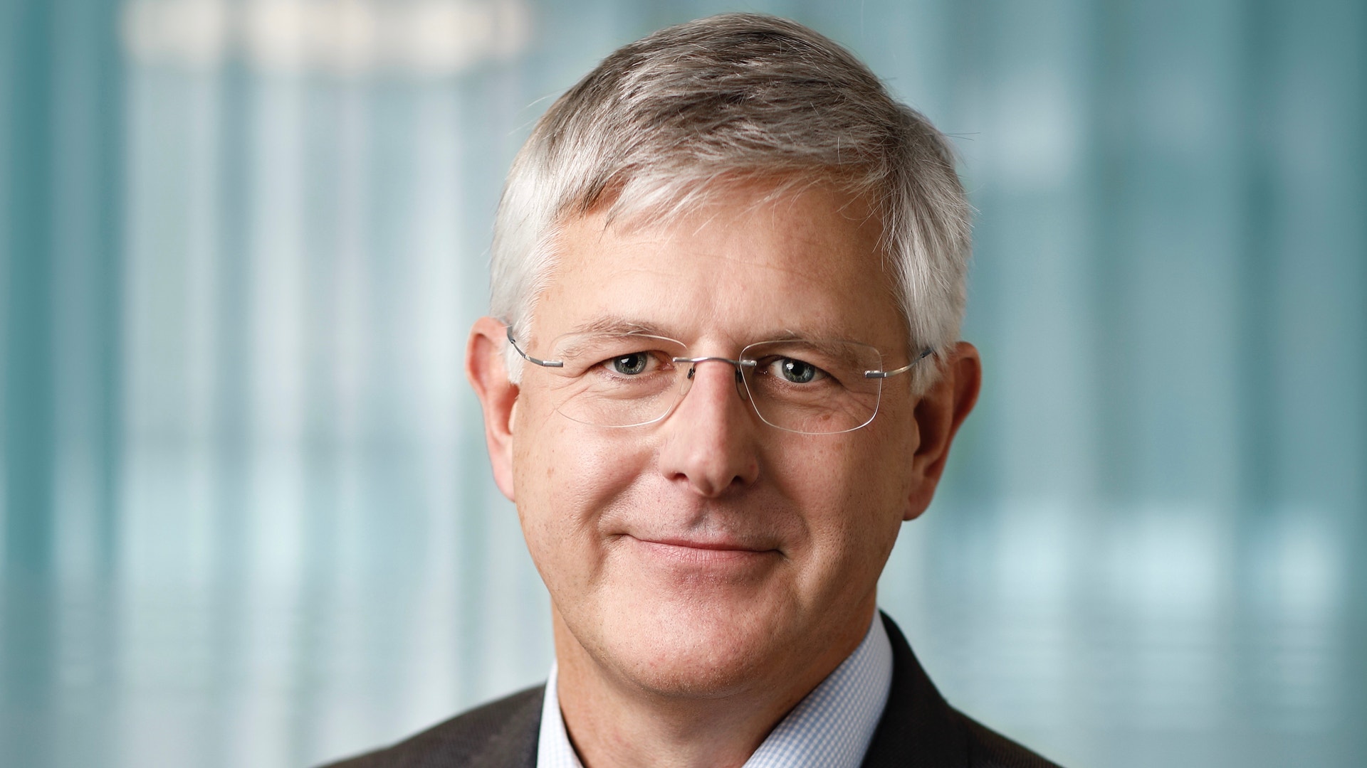 Porträttfoto av en man i affärskläder med glasögon mot en suddig kontorsbakgrund.