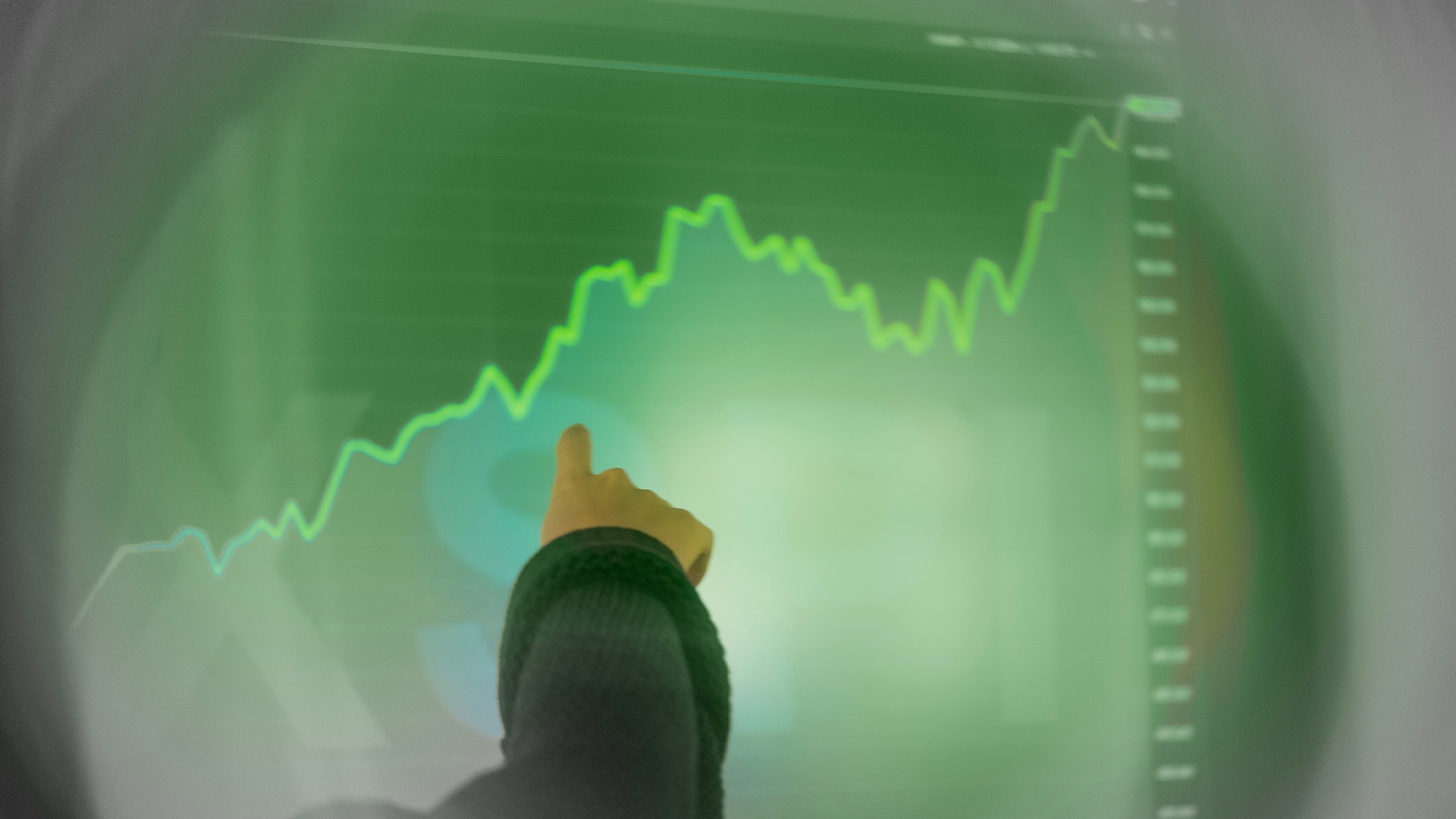 Person pekar på en grön aktiekurs-graf som visar en stigande trend