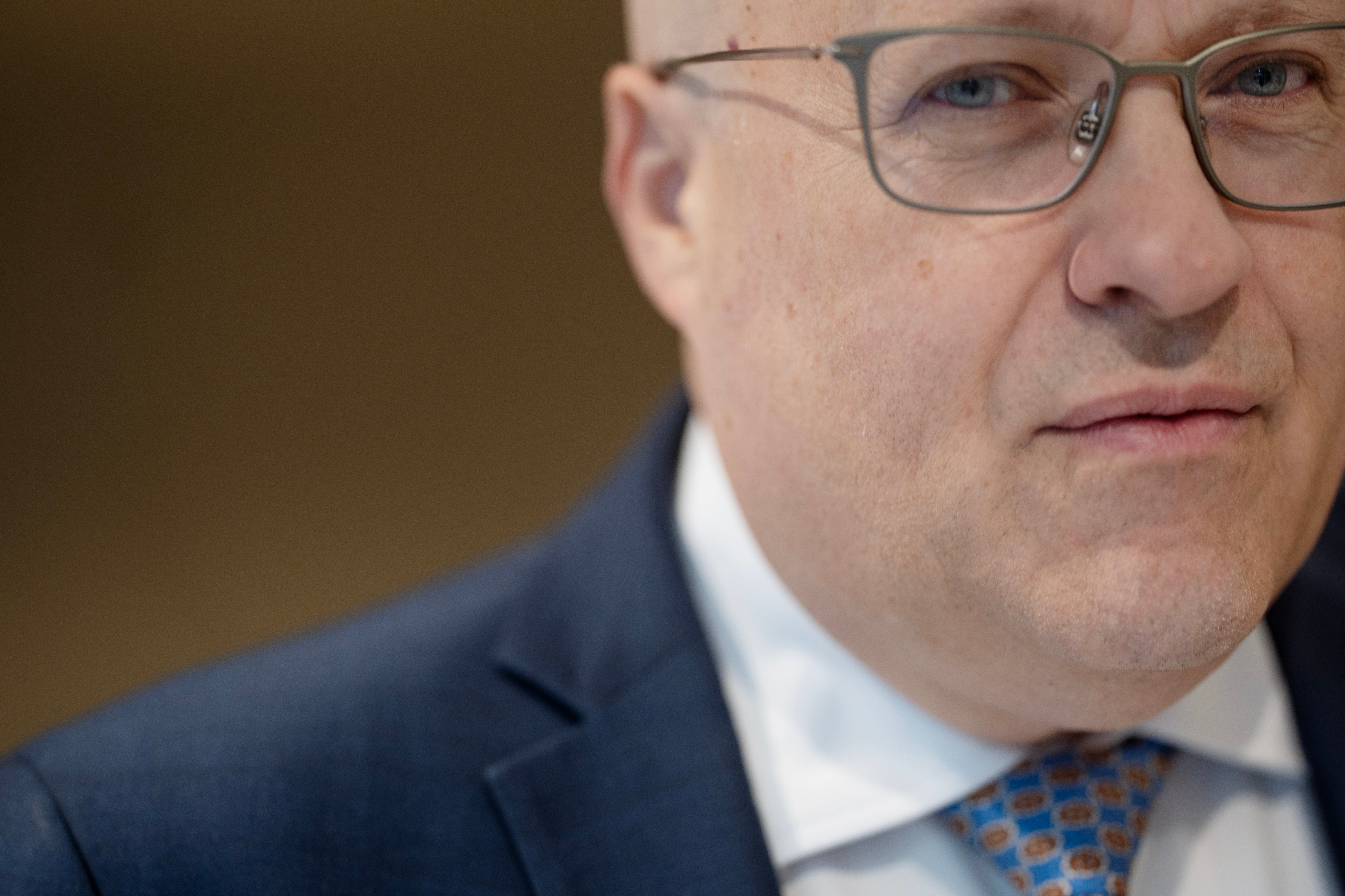 Porträtt av en man med glasögon, iklädd mörkblå kostym och blå slips.