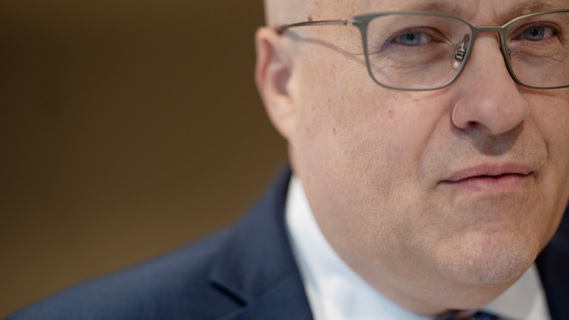 Porträtt av en man med glasögon, iklädd mörkblå kostym och blå slips.